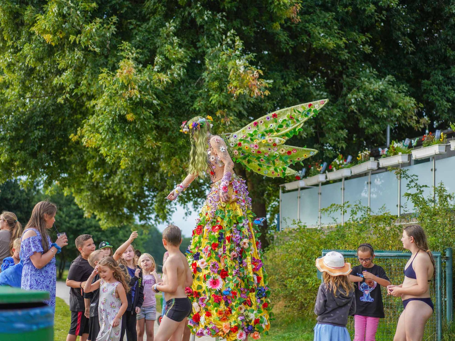 Fee im Blumenkostüm interagiert im Freien mit einer Gruppe von Kindern.