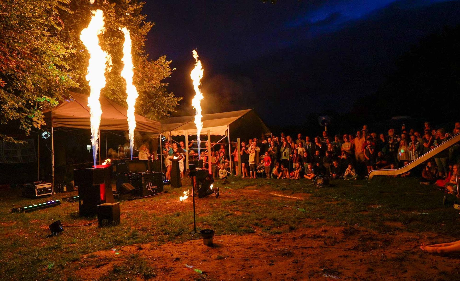Feuerkünstler in der Nacht; große Flammen schlagen aus, die Menge schaut in der Nähe eines Zeltes zu.
