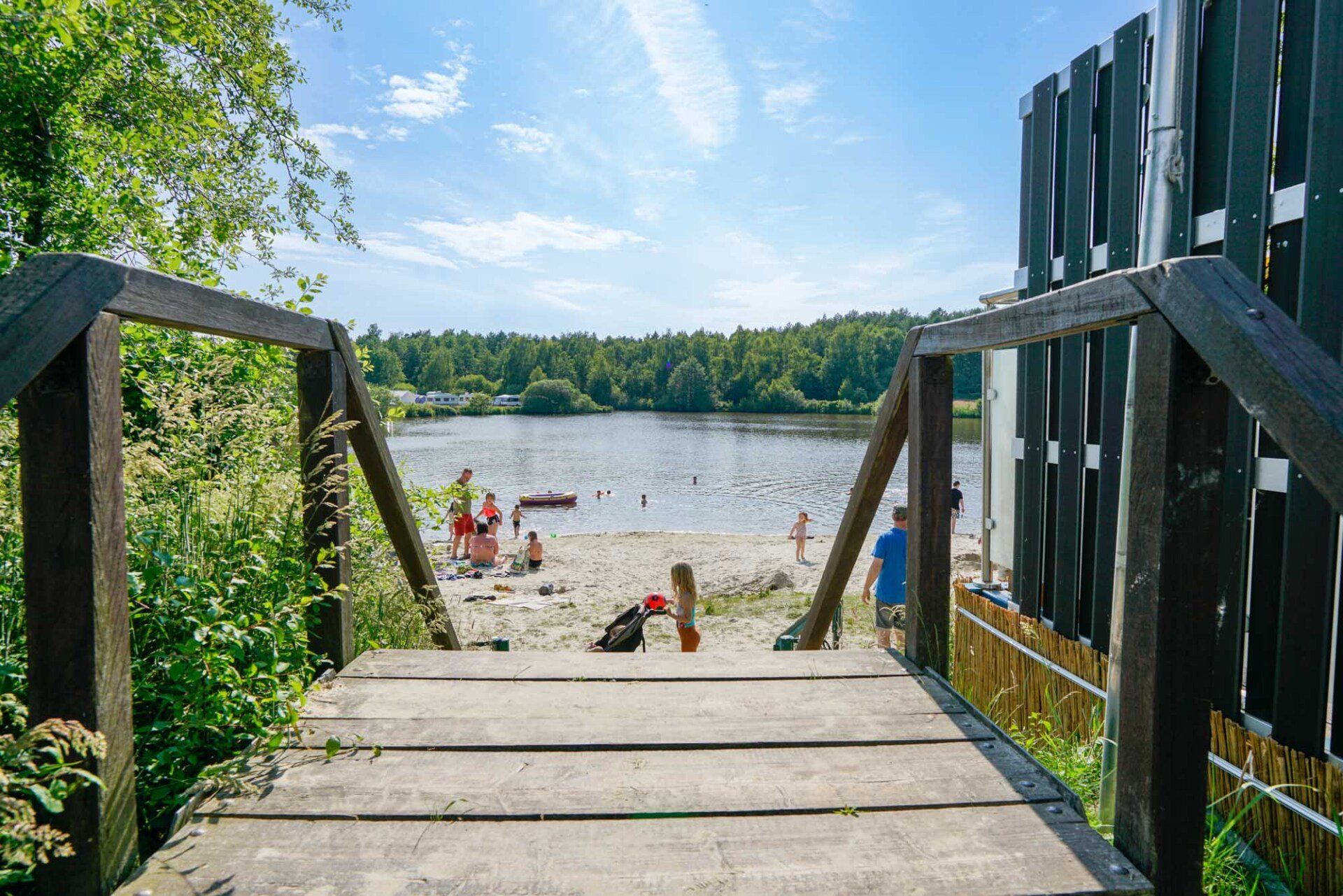 Holzstufen führen zu einem Sandstrand und einem See mit Menschen.