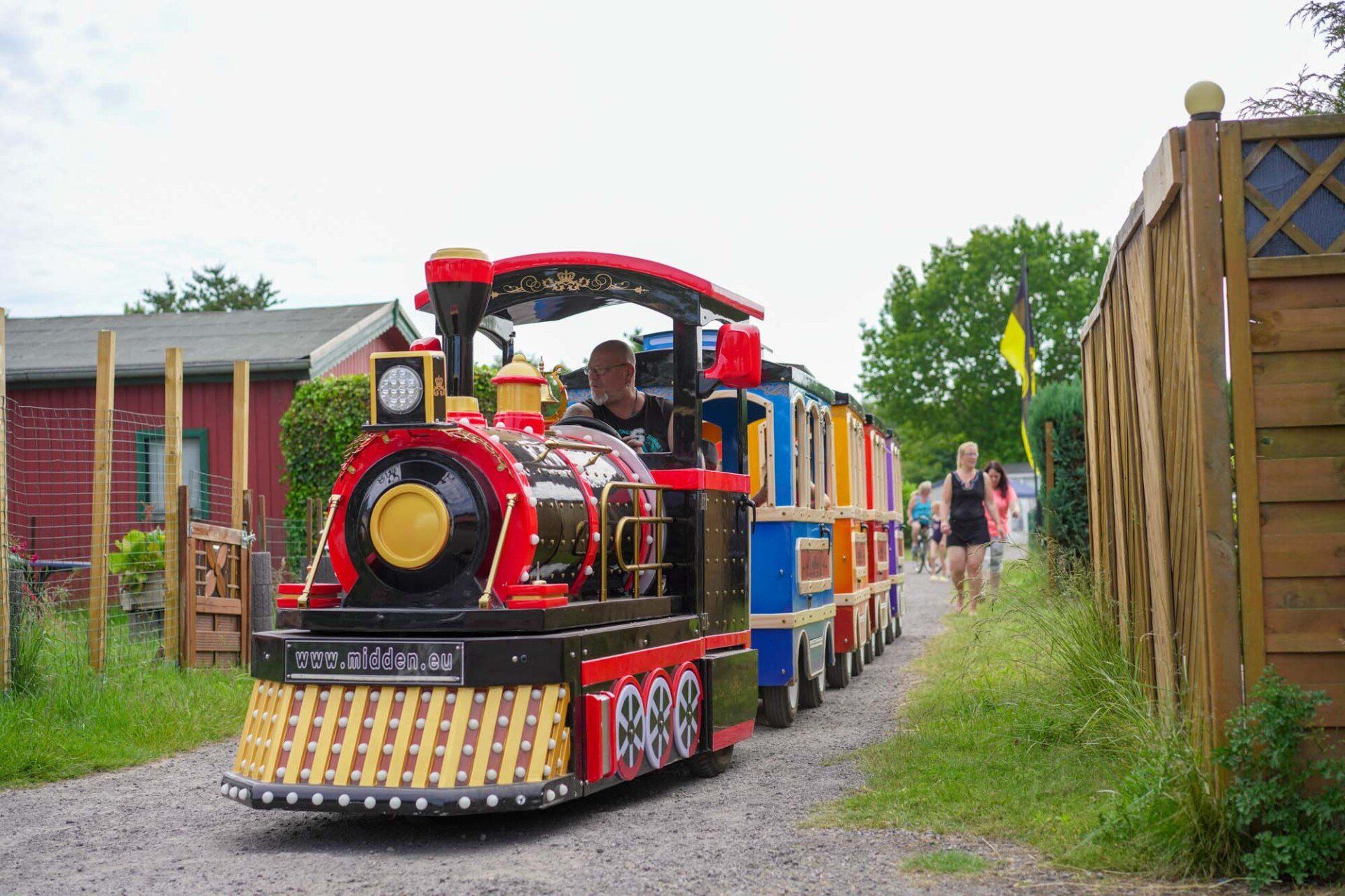 Spielzeugeisenbahn mit Passagieren auf einem Schotterweg. 