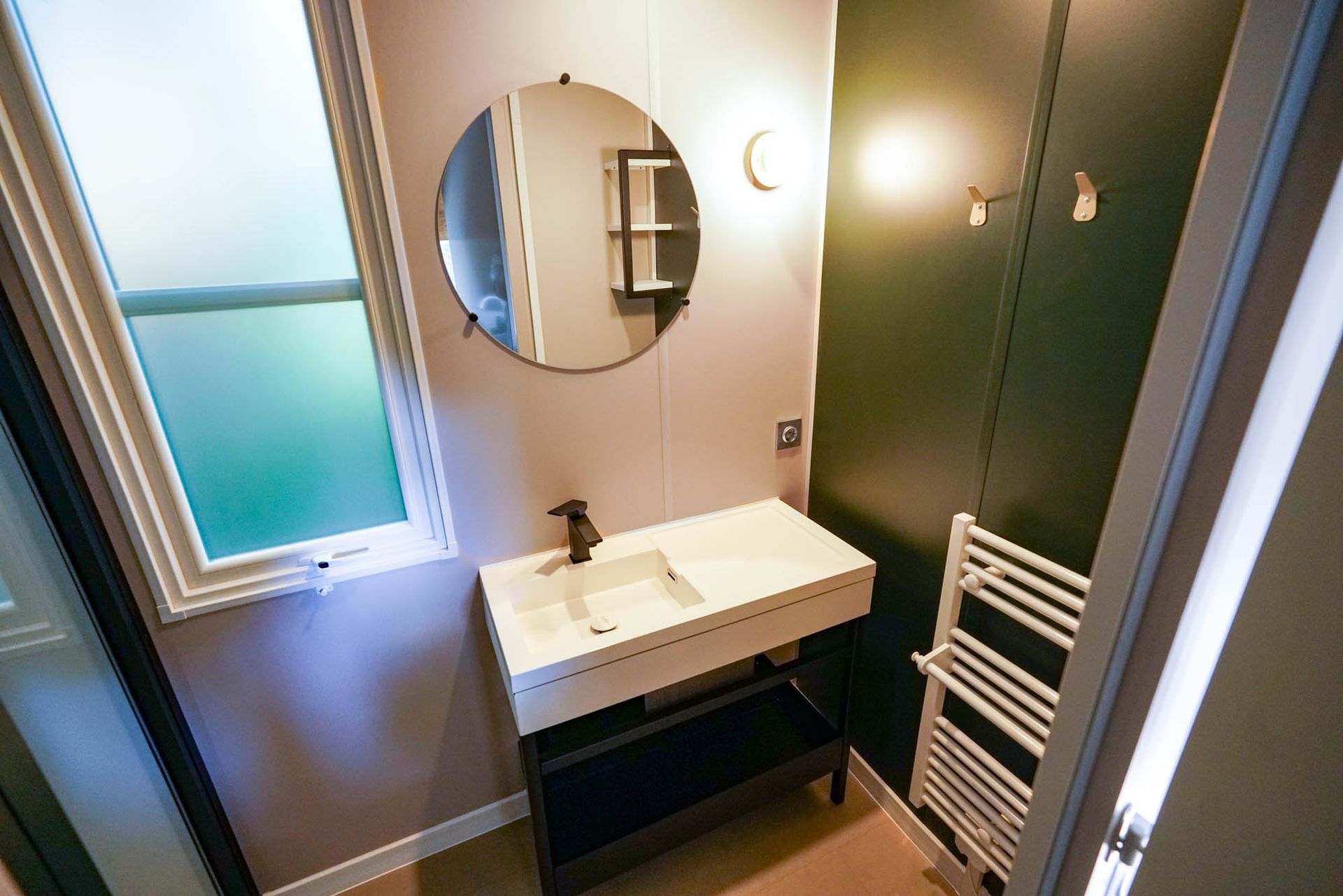 Badezimmer mit weißem Waschbecken, rundem Spiegel, grüner Wand und Handtuchhalter.