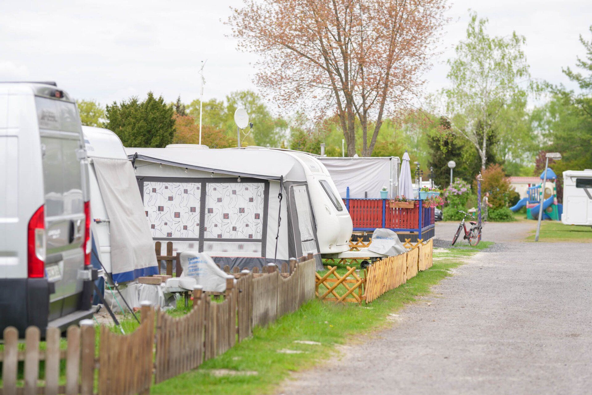 Wohnmobilpark mit Wohnwagen und Zäunen, im Hintergrund Gras, Bäume und Himmel