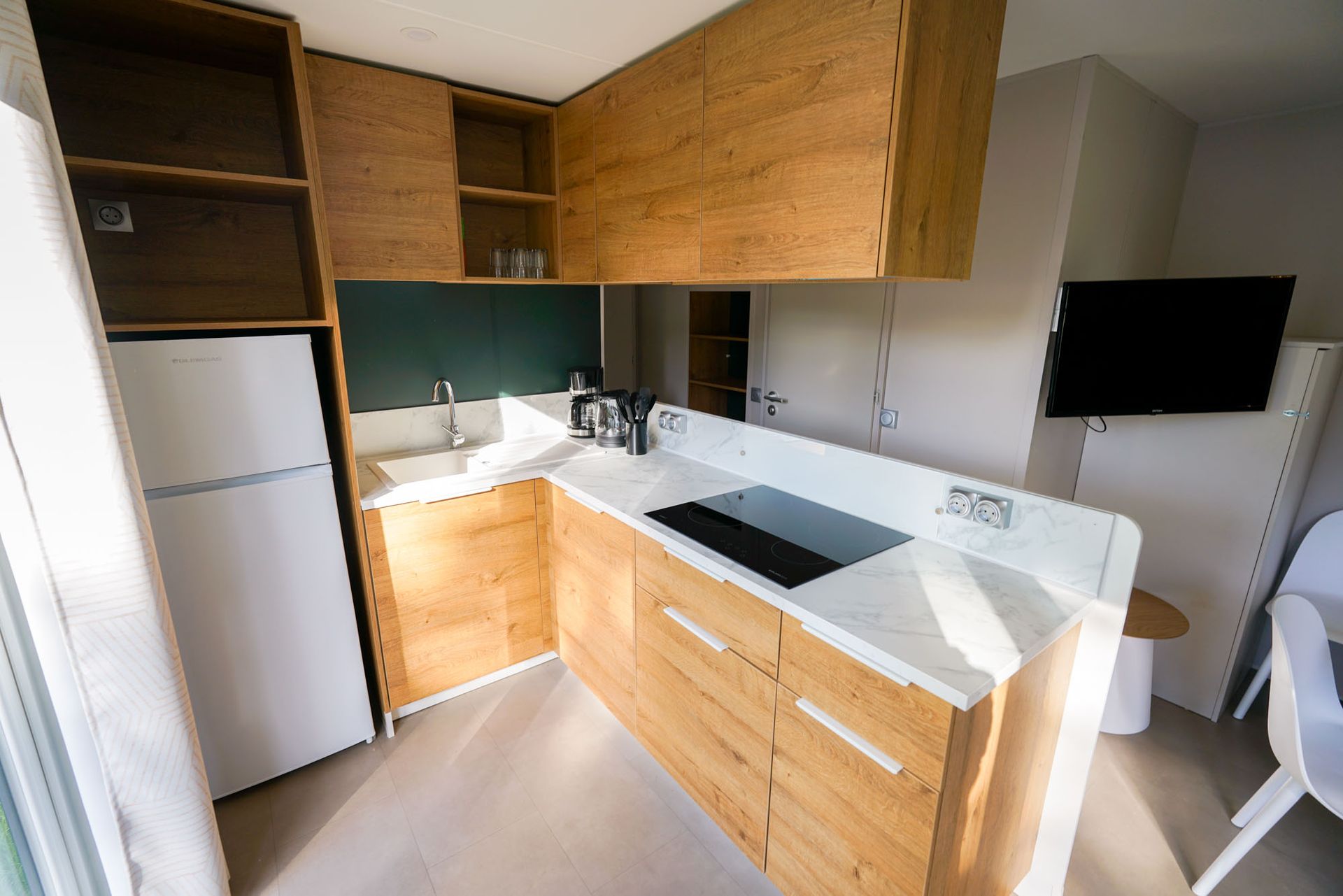 Kleine moderne Küche mit Holzschränken, weißen Arbeitsplatten und Kühlschrank. 
