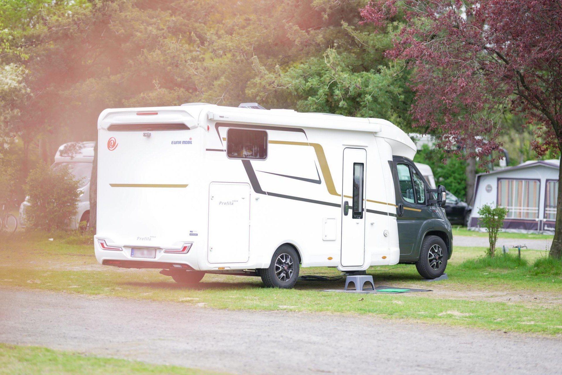 Weißes Wohnmobil auf Campingplatz, im Hintergrund Bäume.