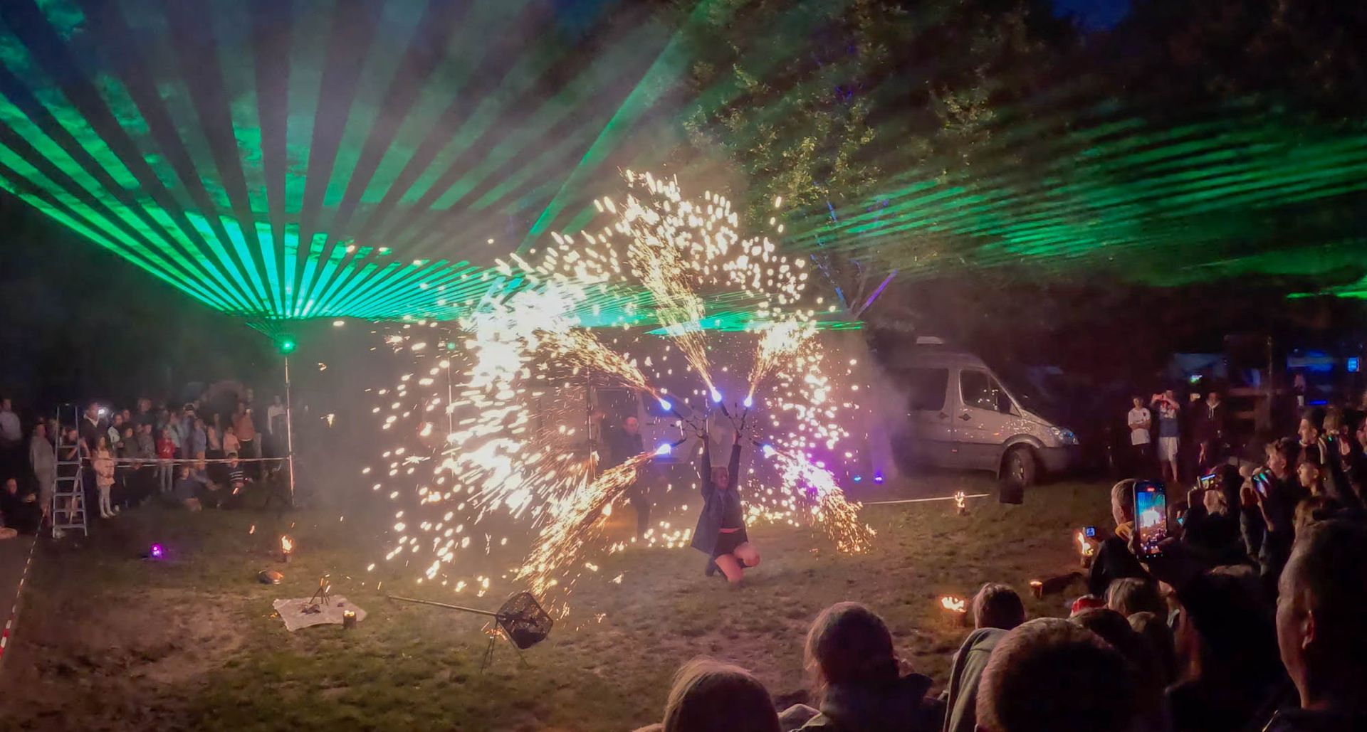 Feuerkünstler umgeben von explodierender Pyrotechnik, grüne Laserlichter über ihm