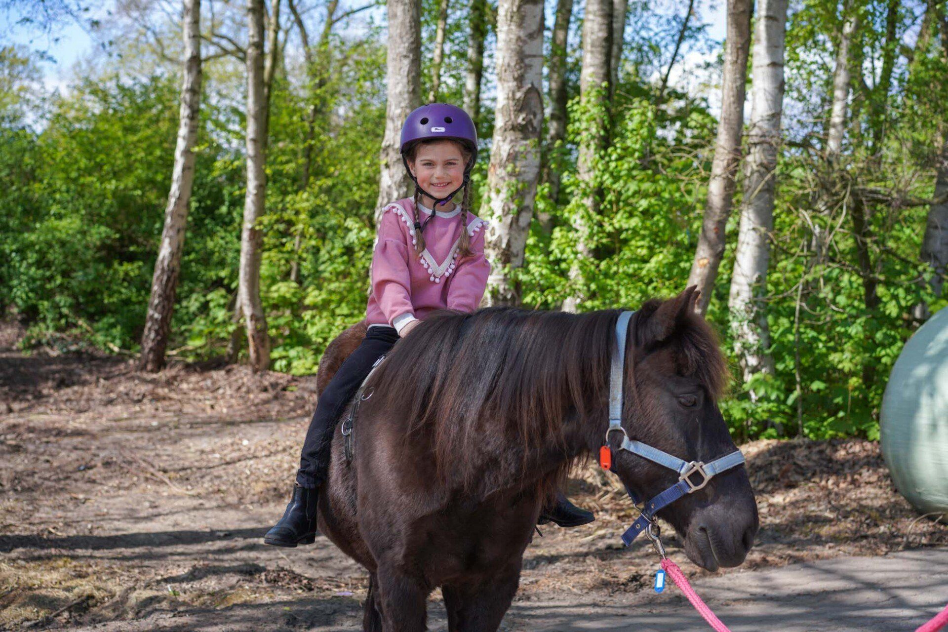 Mädchen mit Helm reitet im Freien auf einem dunklen Pony