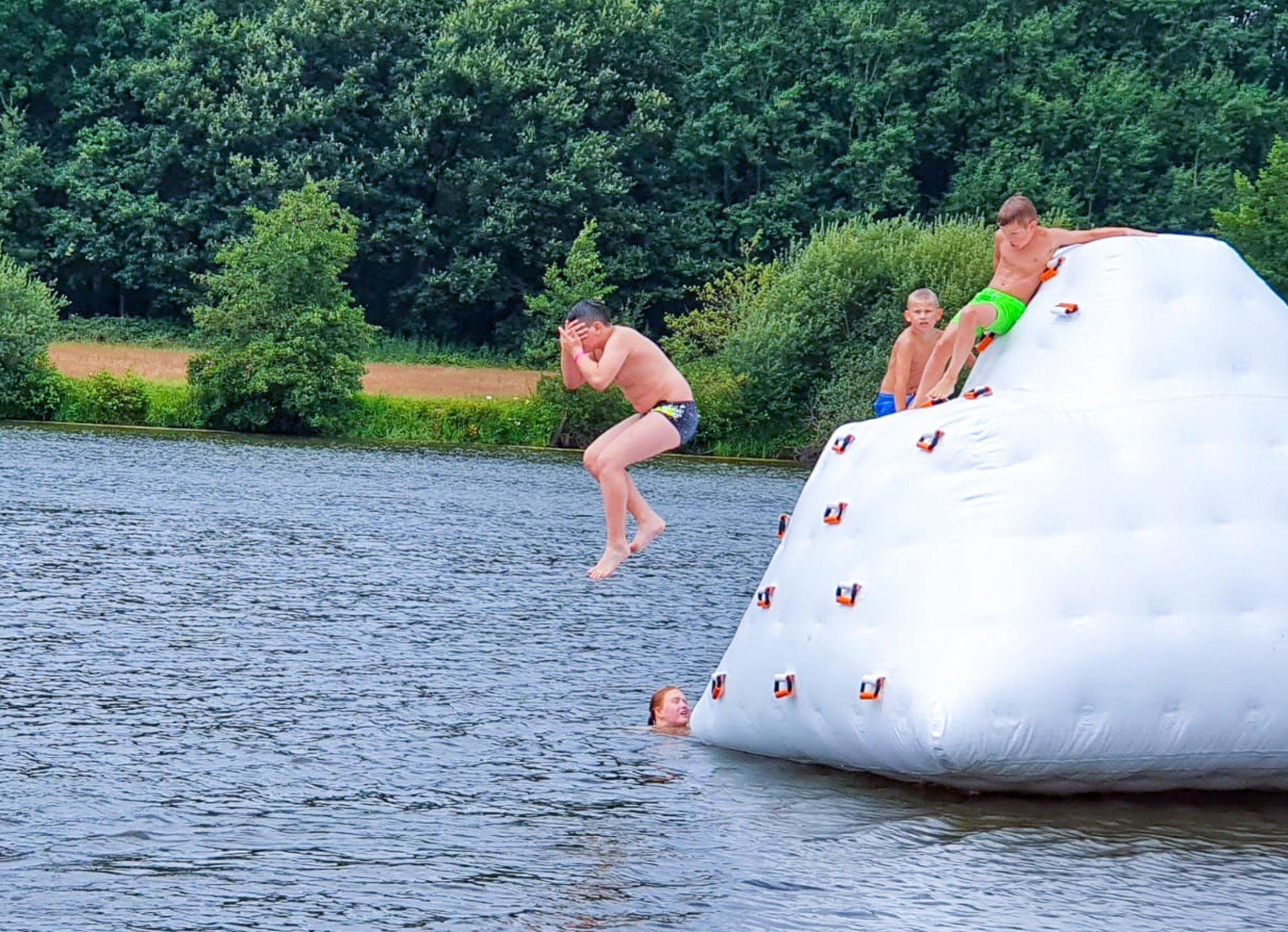 Junge springt von aufblasbaren Eisberg in See. Zwei andere Jungen sitzen oben drauf.