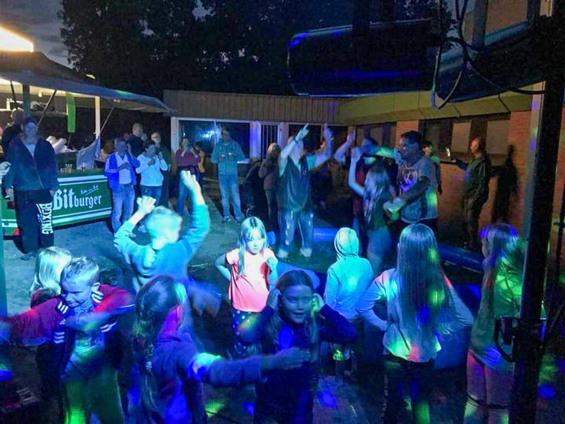 Kinder tanzen auf einer Party im Freien, die mit bunten Lichtern  beleuchtet ist.