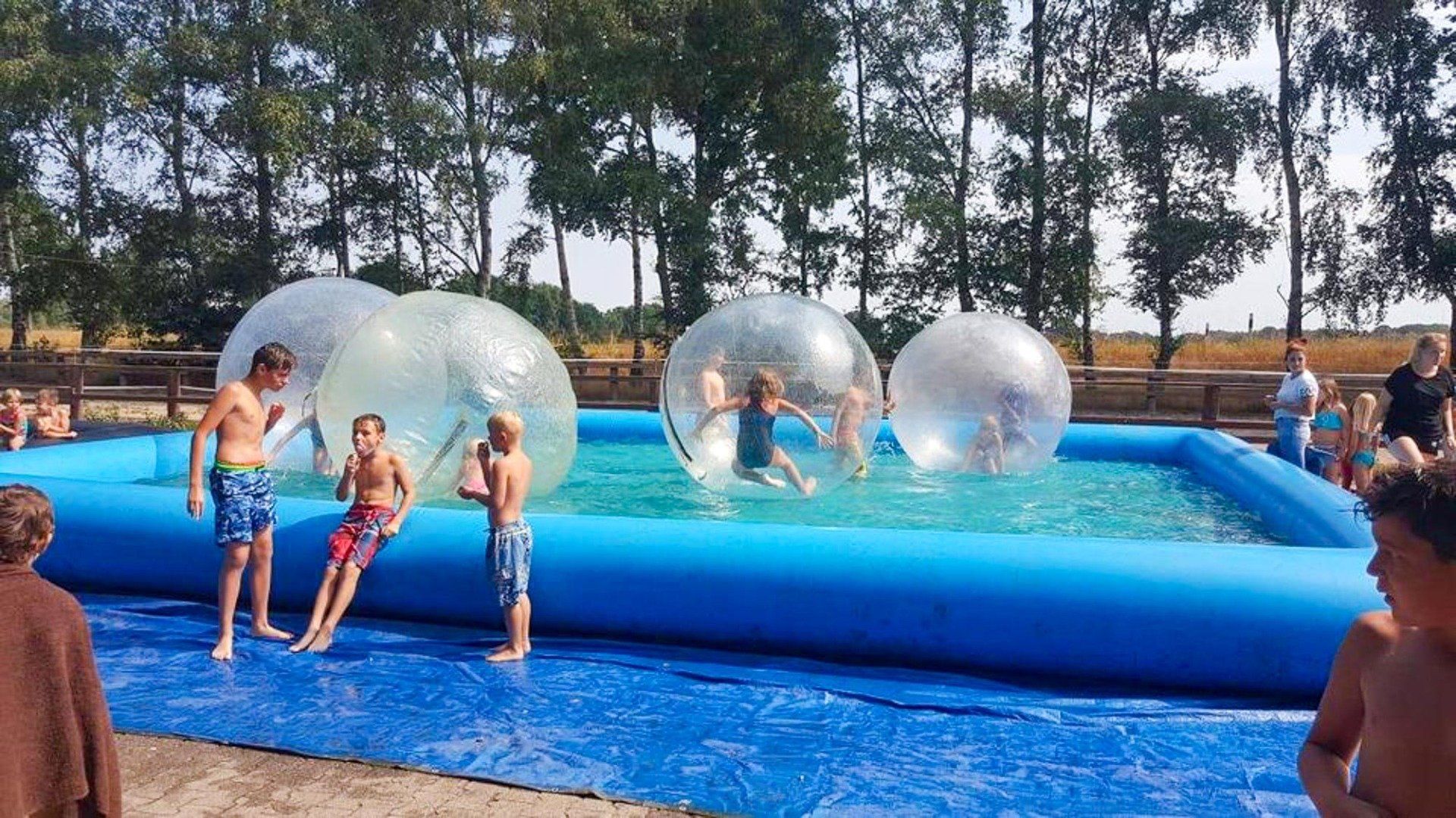 Kinder spielen in einem mit Wasser gefüllten aufblasbaren Pool in durchsichtigen Seifenblasenbällen.