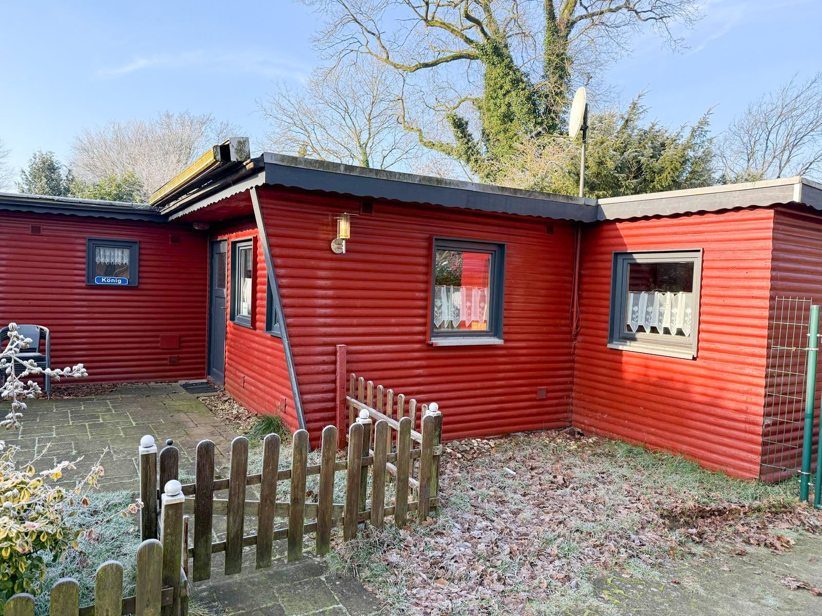 Rote Holzhütte mit einem kleinen Holzzaun und gefrorenem Boden an einem sonnigen Tag.