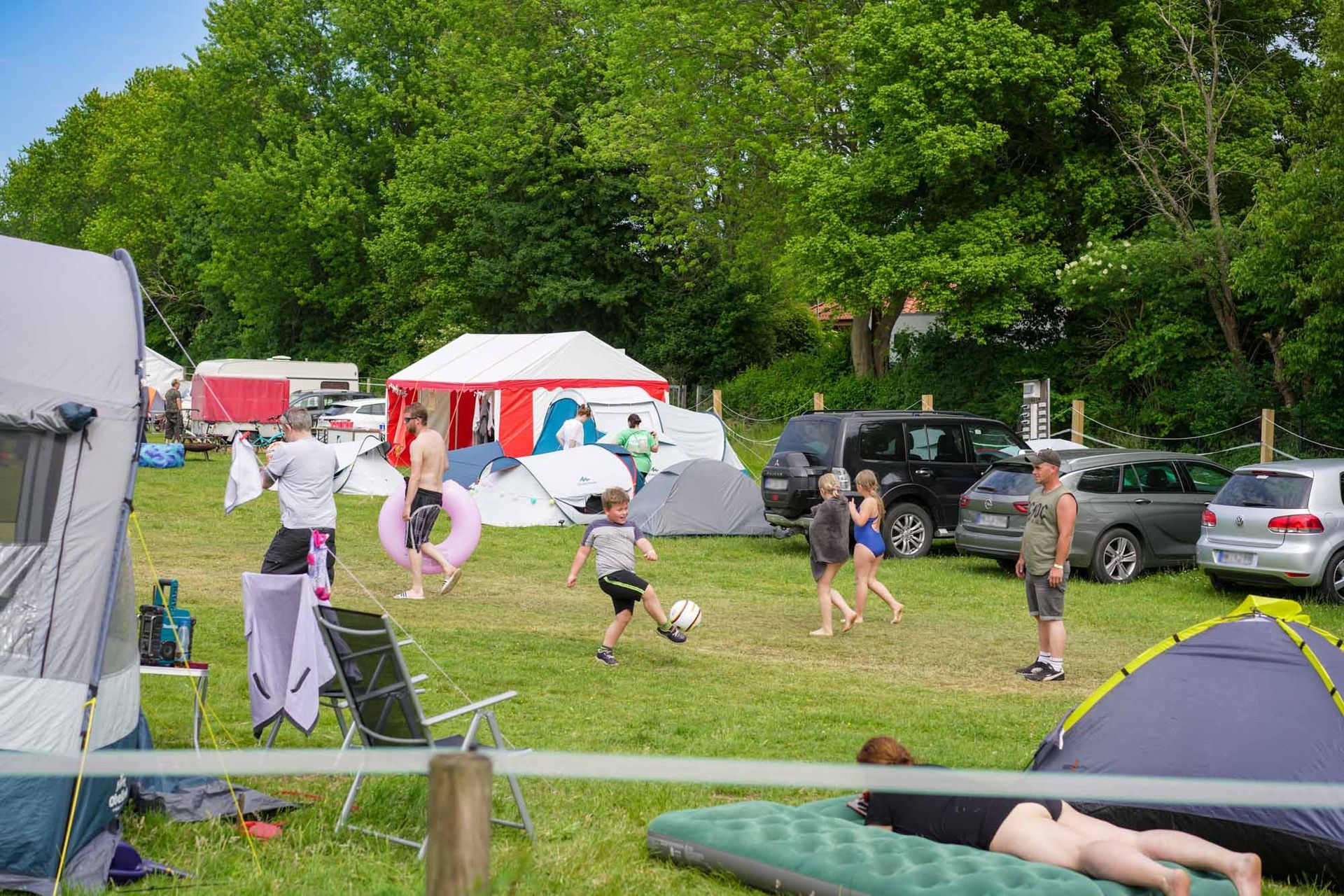 Menschen spielen Fußball in der Nähe von Zelten und Autos auf einer Wiese
