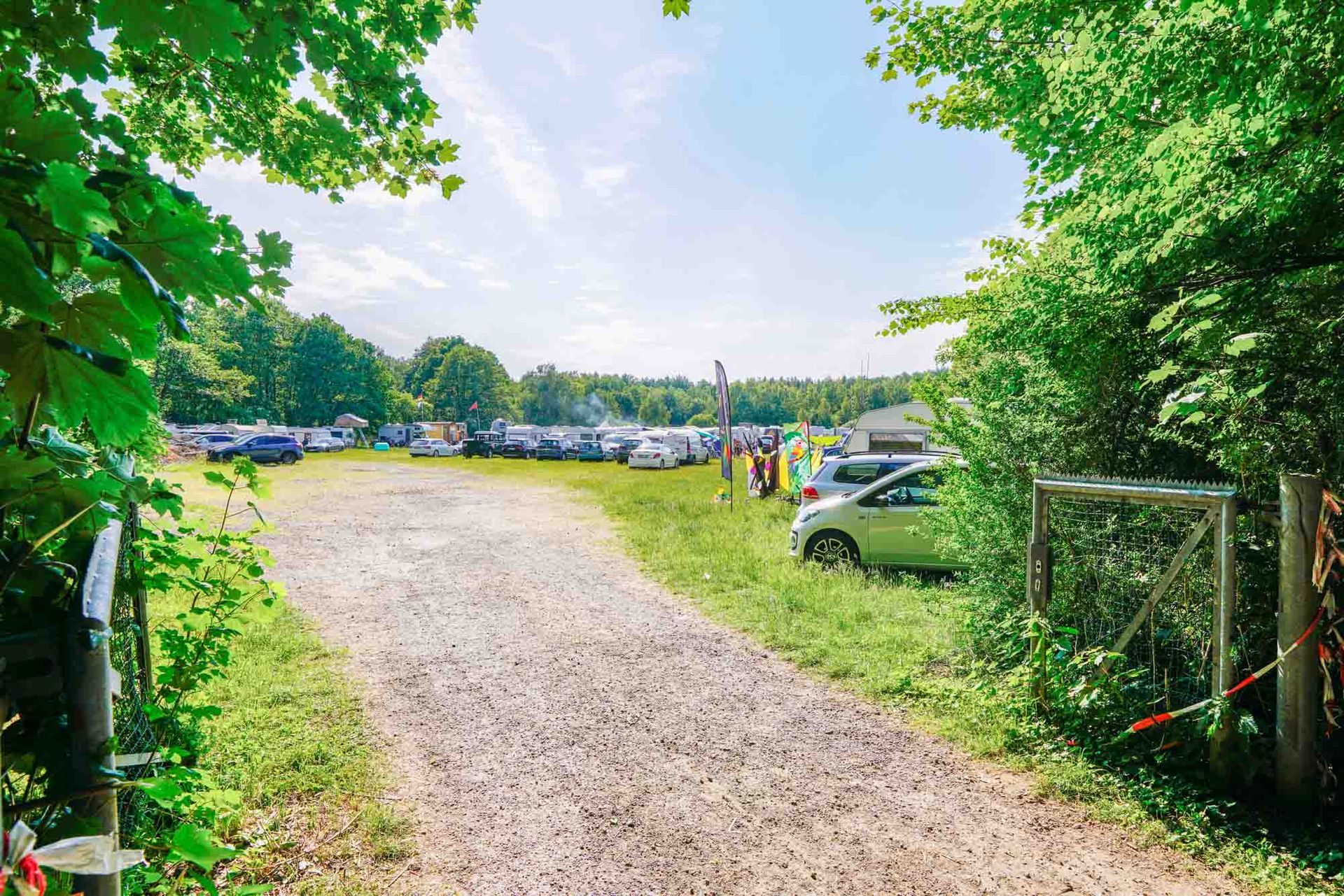 Ein Schotterweg führt zu einem Parkplatz mit Autos und Bäumen
