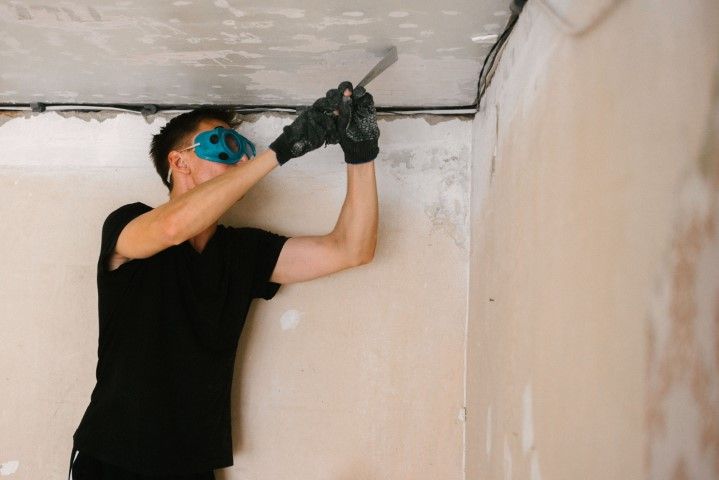 Person wearing safety glasses and gloves using a tool on a ceiling in a room.