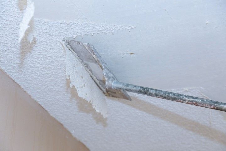 A metal scraper removing peeling paint from a white wall.