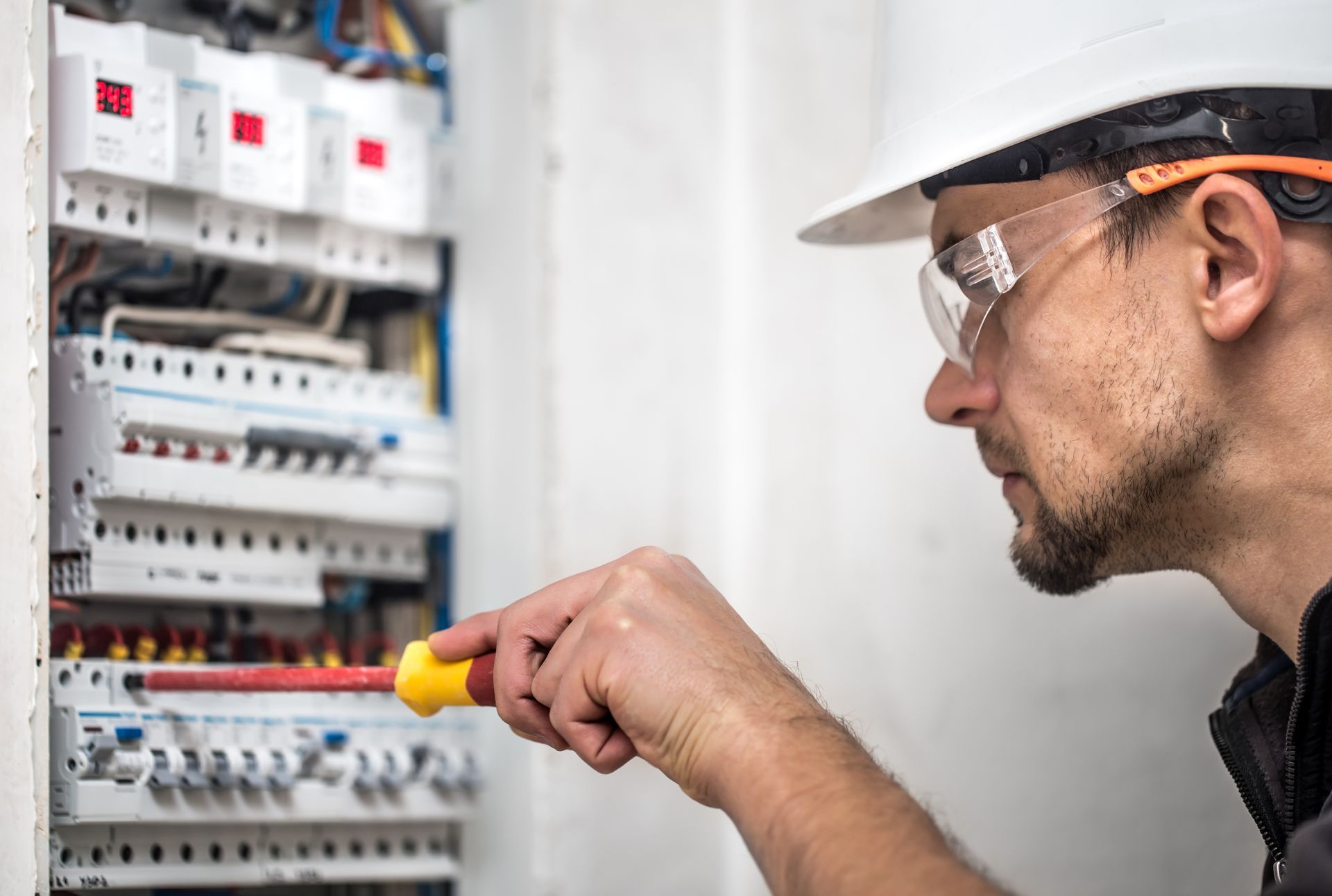 An electrician is working on an electrical box with a screwdriver.