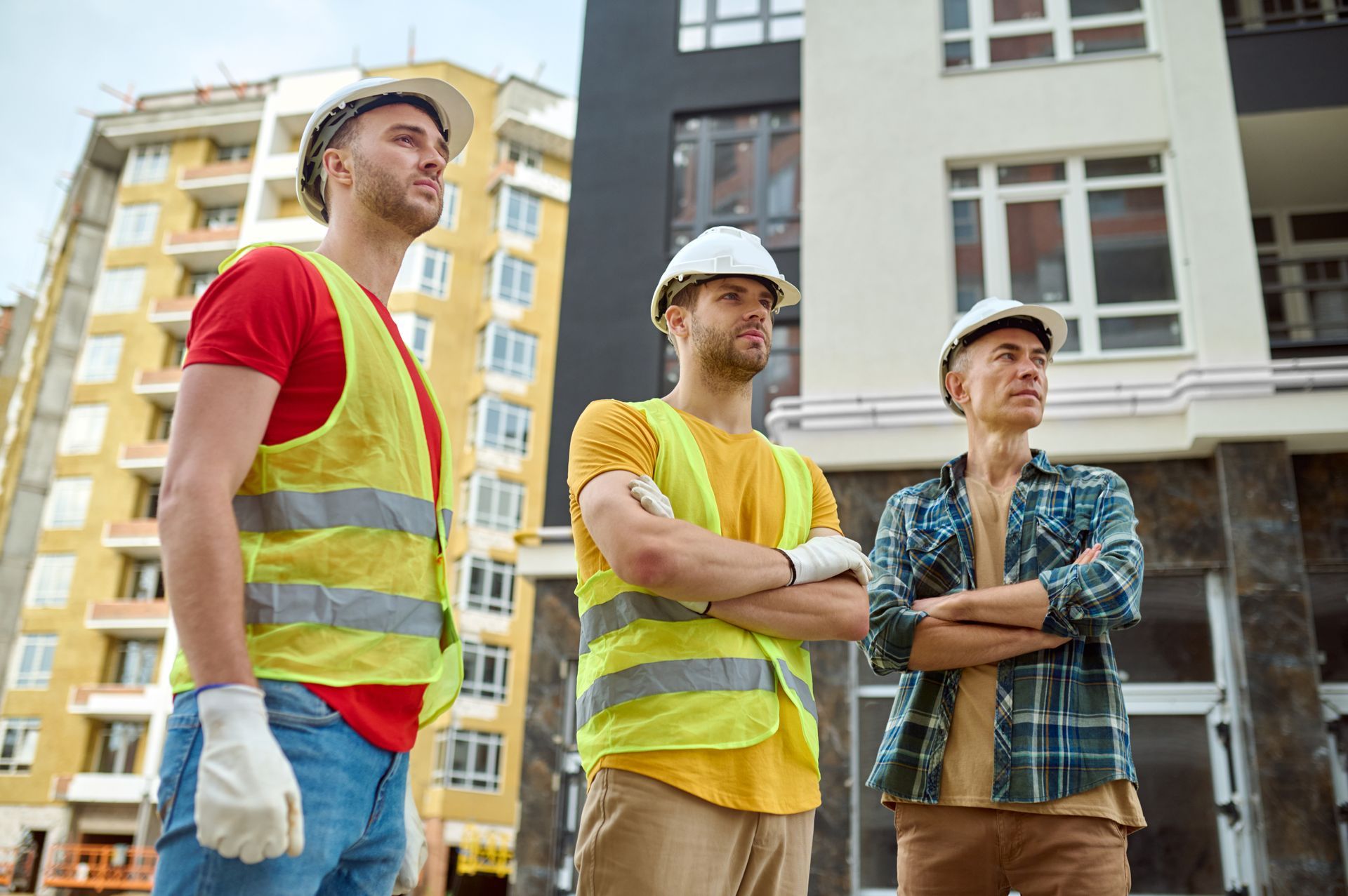 Three construction workers are standing in front of a building under construction.