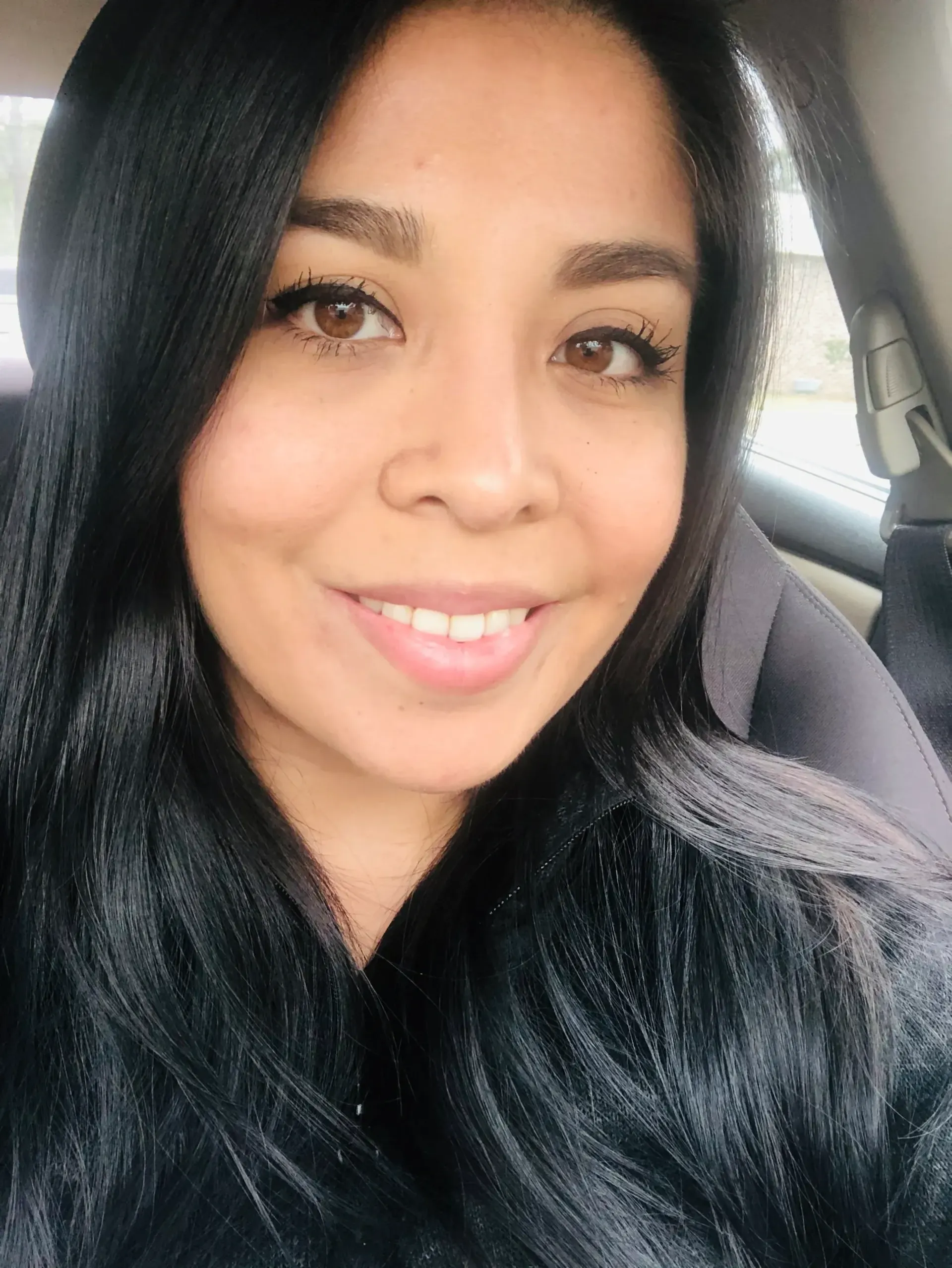 Jhoanna Corona, a woman with long black hair, smiling while seated in a car.