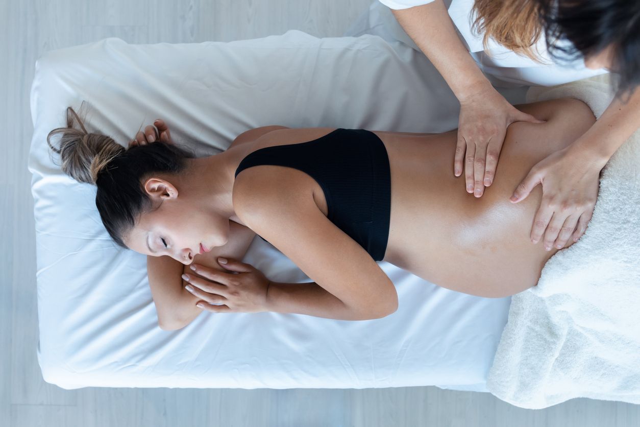 A pregnant woman is getting a massage on a bed.