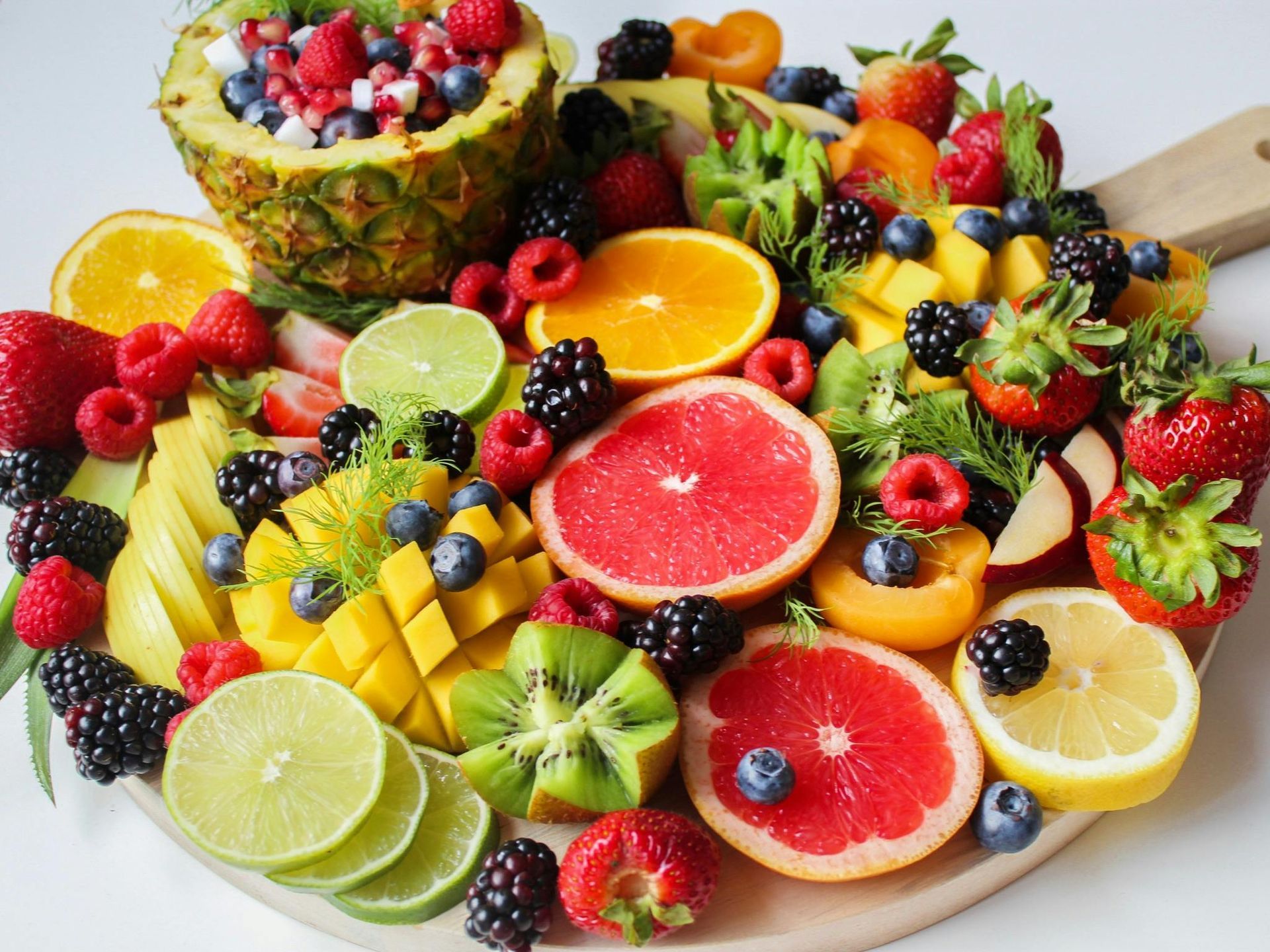 Colorful fruit platter on a wooden board: pineapple, berries, citrus, mango, kiwi.