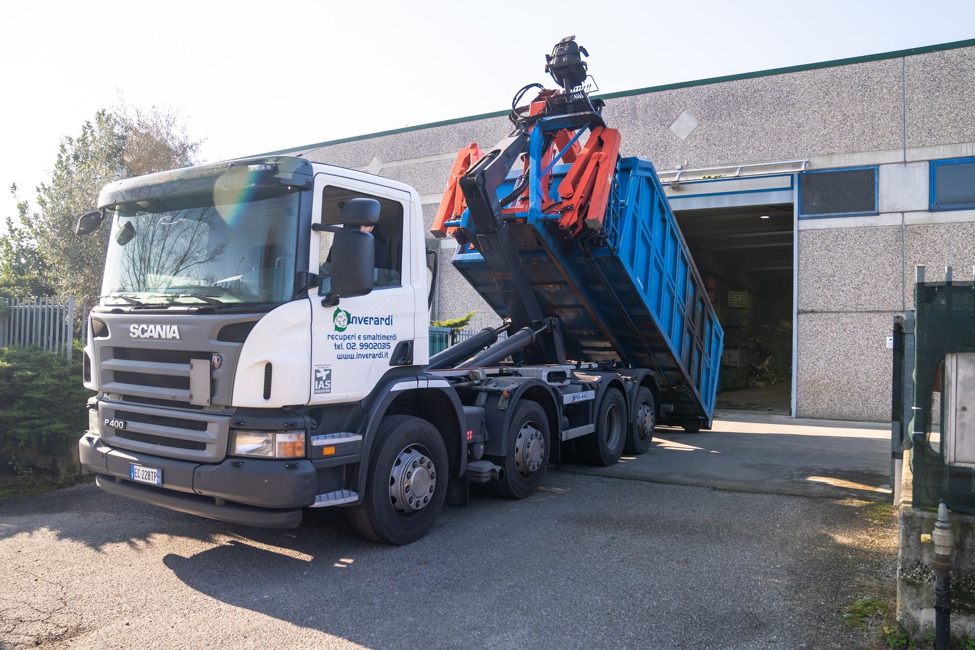Camion Scania bianco che solleva un cassonetto blu fuori da un edificio