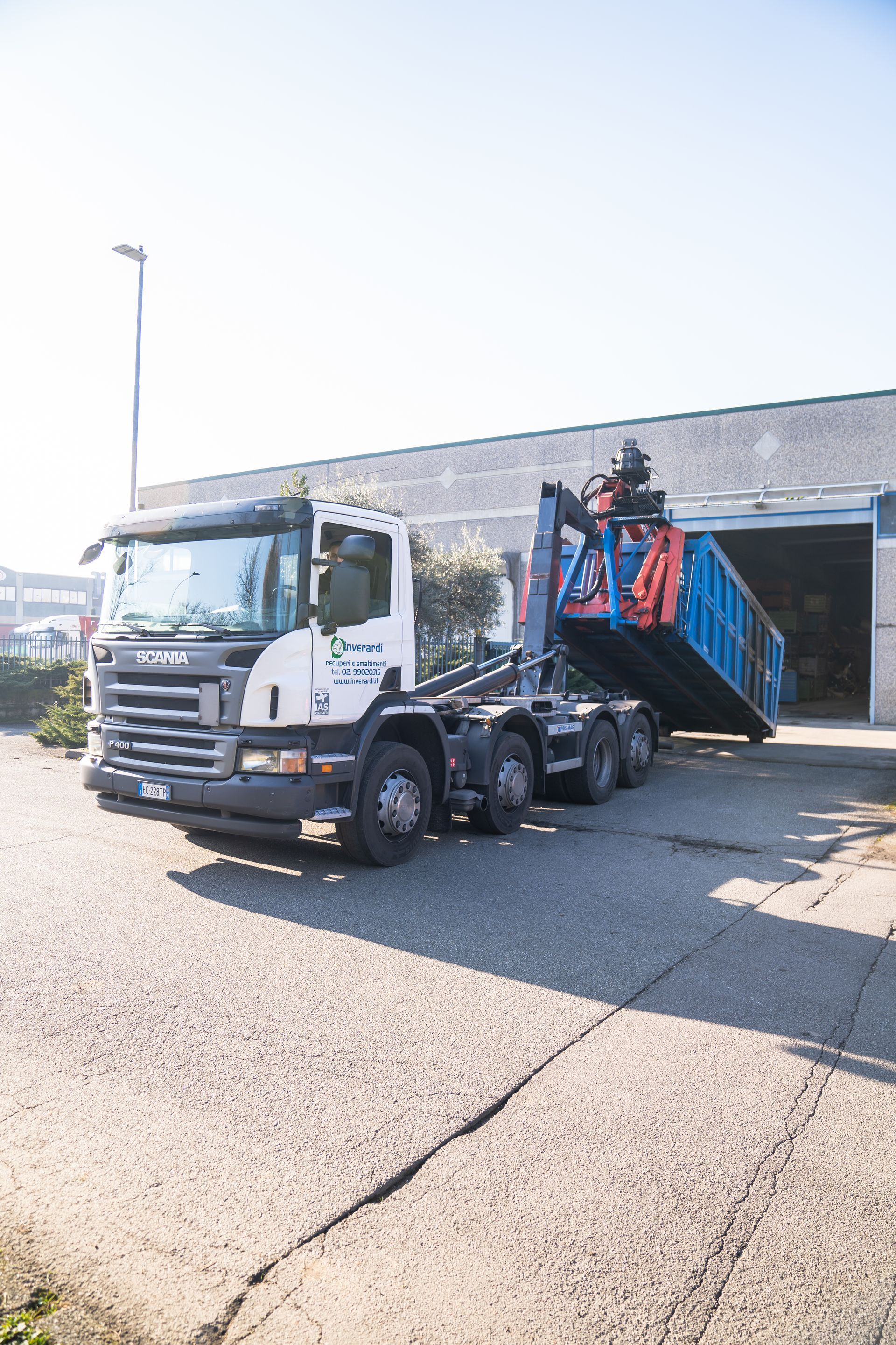 Camion bianco con un container blu, sollevato vicino a un magazzino 