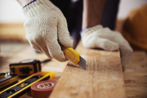 operaio con guanti da lavoro taglia un pezzo di legno con il cutter