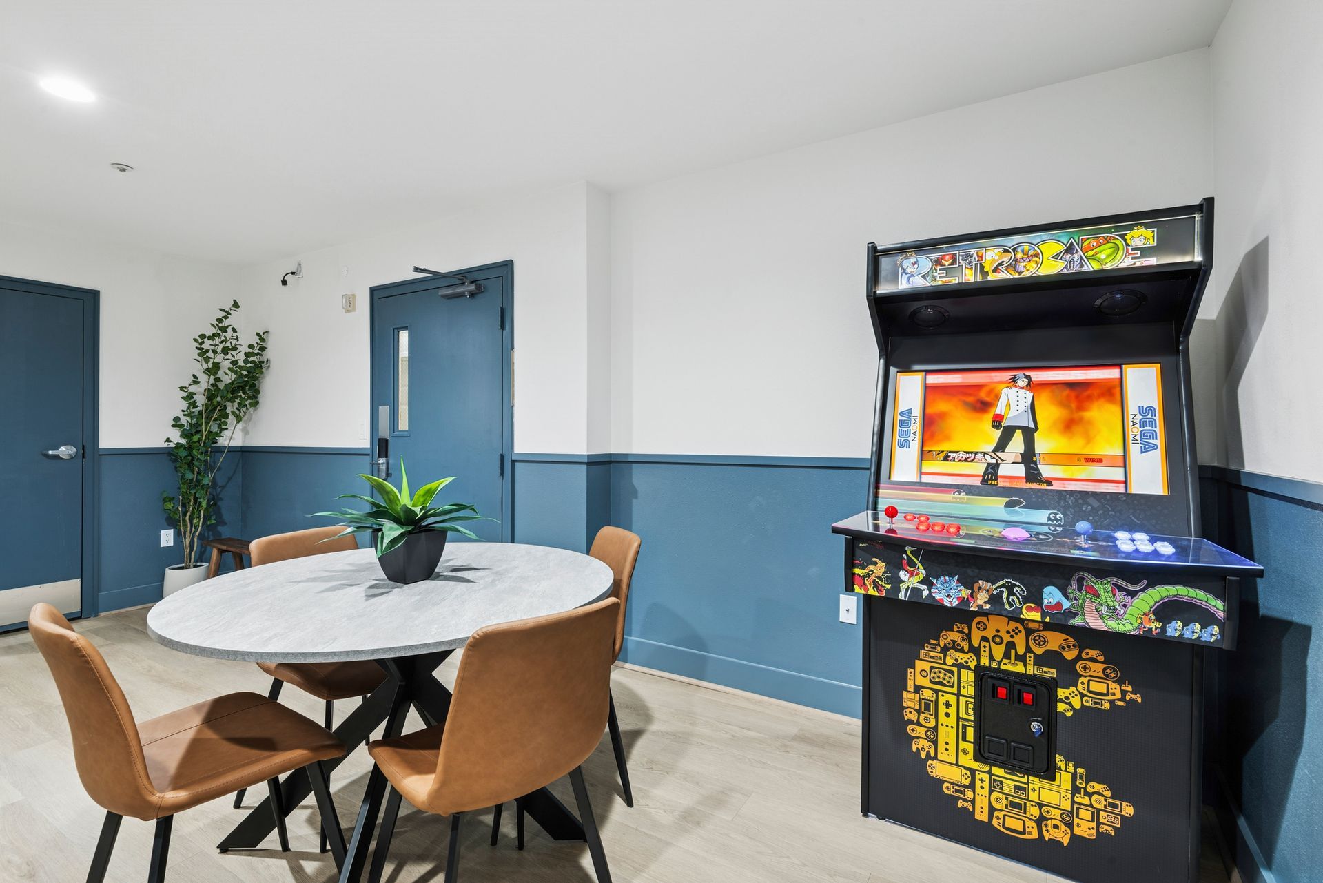Gaming room with an arcade game, round table, chairs, and a blue door.