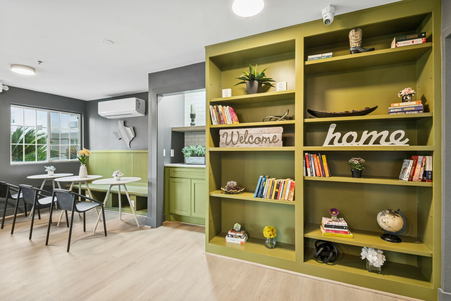 Interior with green bookshelves and dining area. Light wood floor, white walls and accent colors.