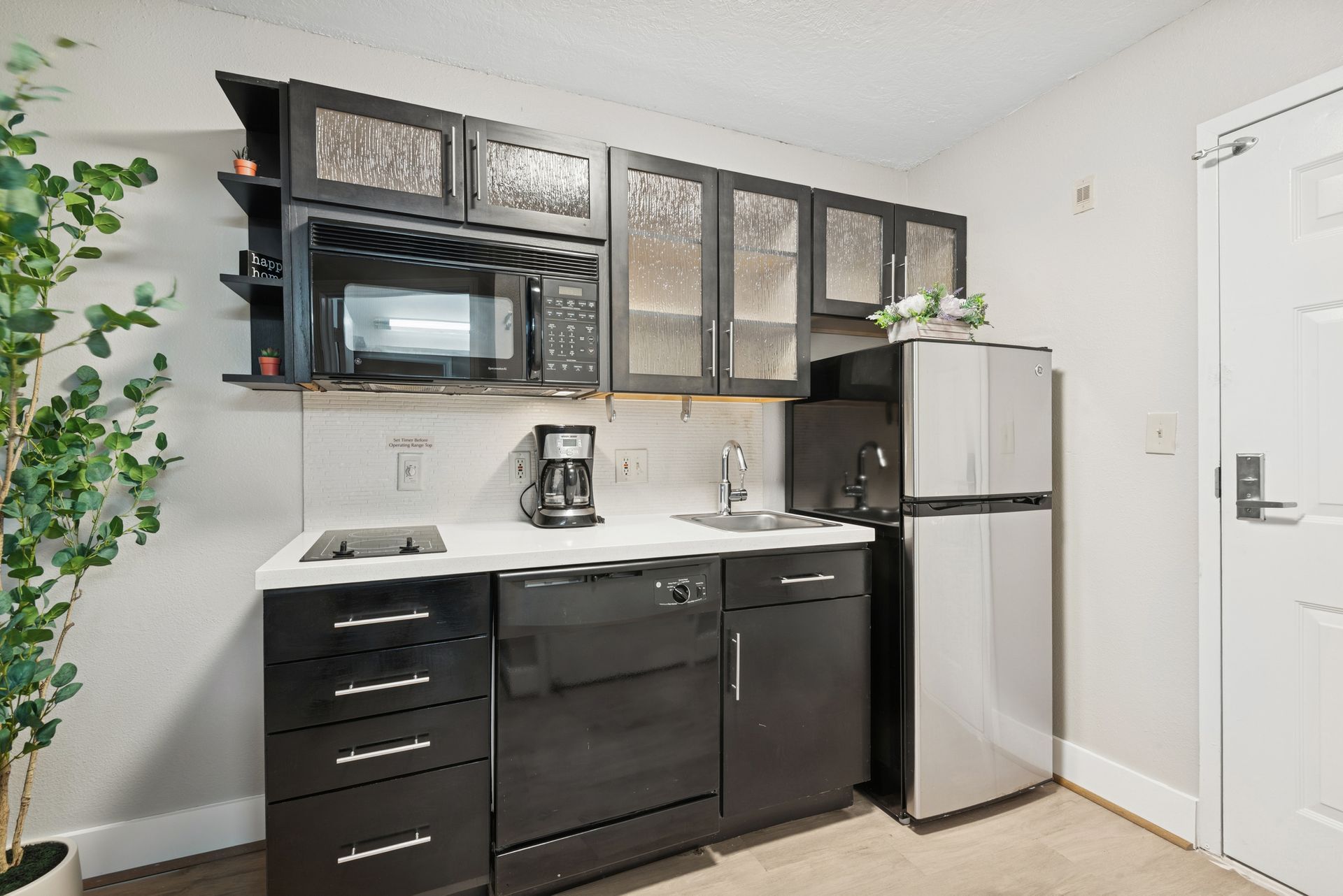 Small kitchenette with black cabinets, microwave, fridge, and sink.