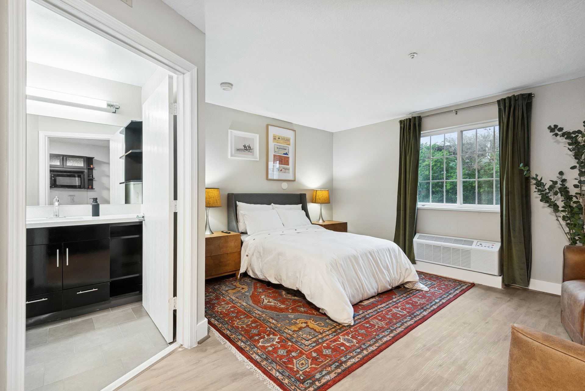 Bedroom with bed, rug, nightstands, and attached bathroom. Window with green curtains.