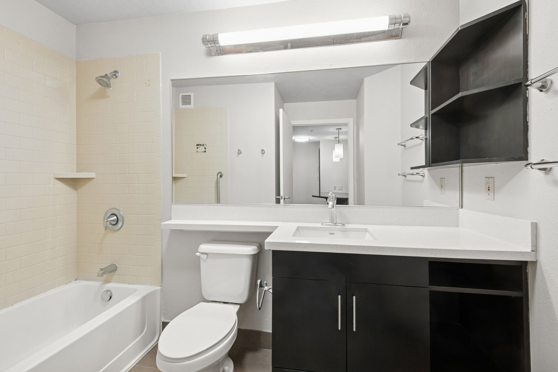 Bathroom with white tub, toilet, and sink. Black vanity. Mirror and medicine cabinet above.