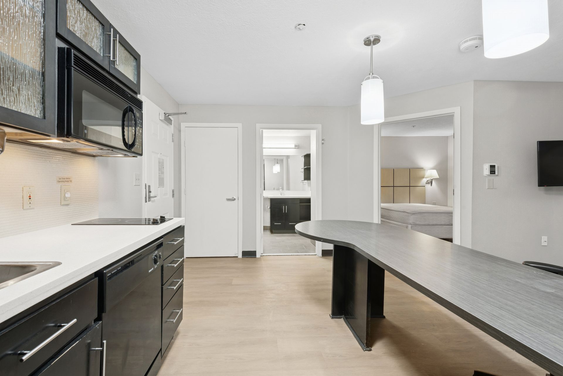 Kitchen area with black cabinets, white countertops, and a long gray table; doorways visible.
