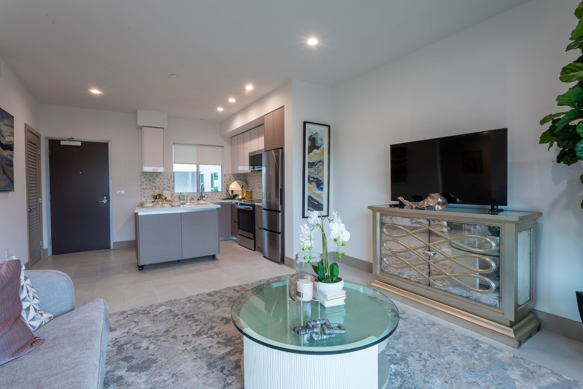 Living room with open kitchen, gray furniture, TV, and large rug.