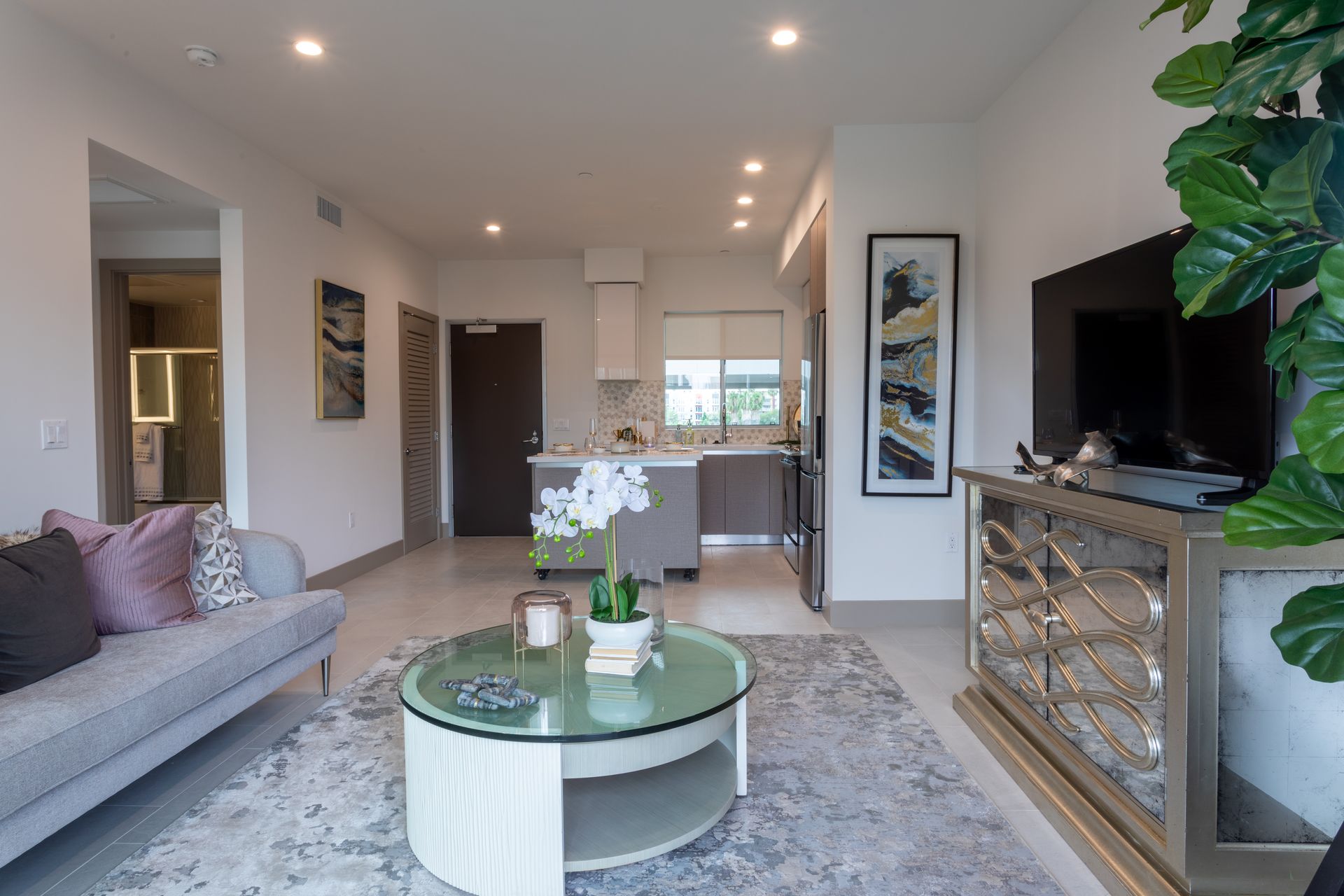 Modern living room with open kitchen, gray sofa, round coffee table, and large TV.