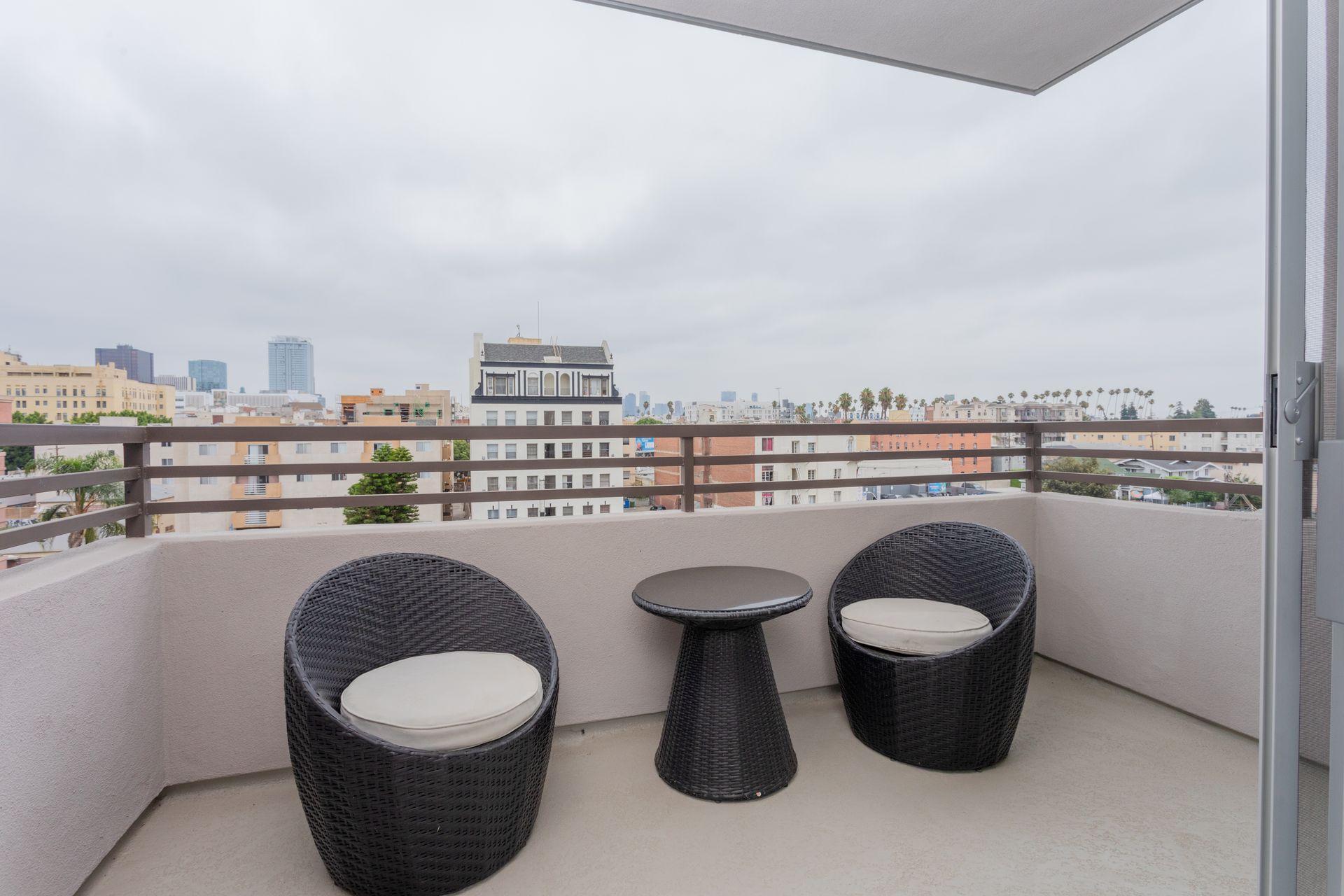 Balcony with two black wicker chairs and small table; city skyline in background.