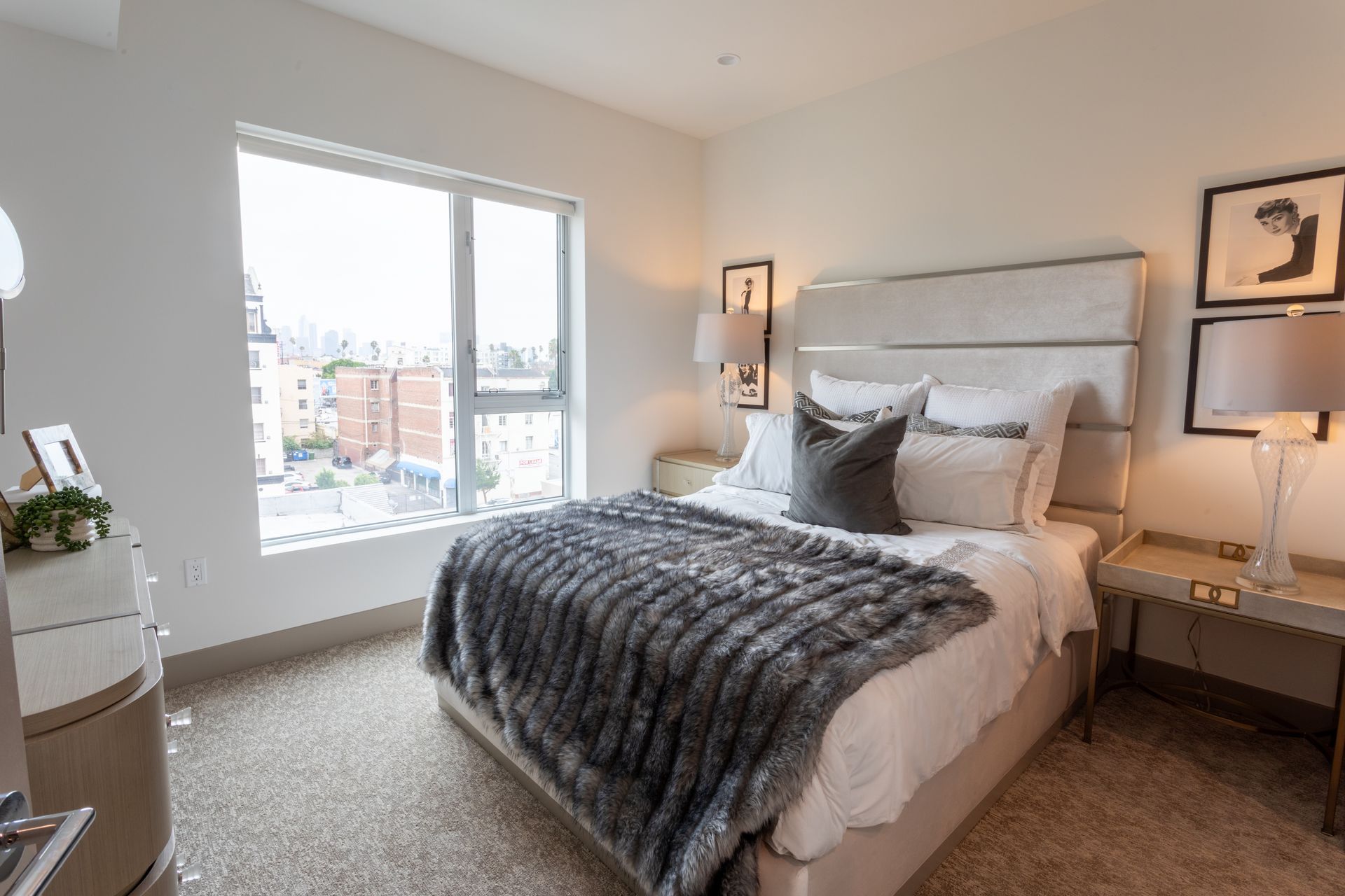 Bedroom with bed, faux fur blanket, window, nightstands, and artwork.
