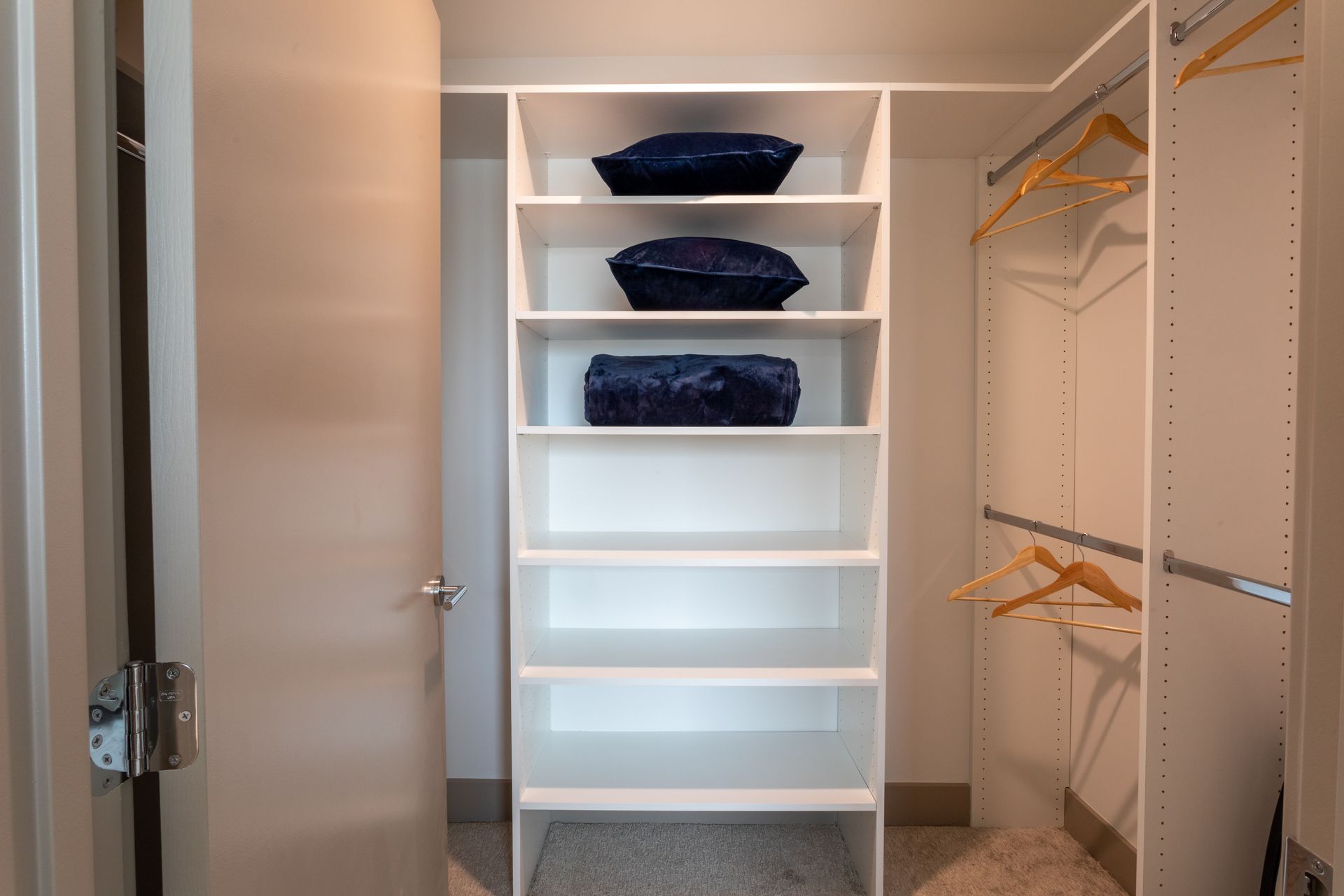 White closet with shelving holding blue pillows and a hanging rod with hangers.
