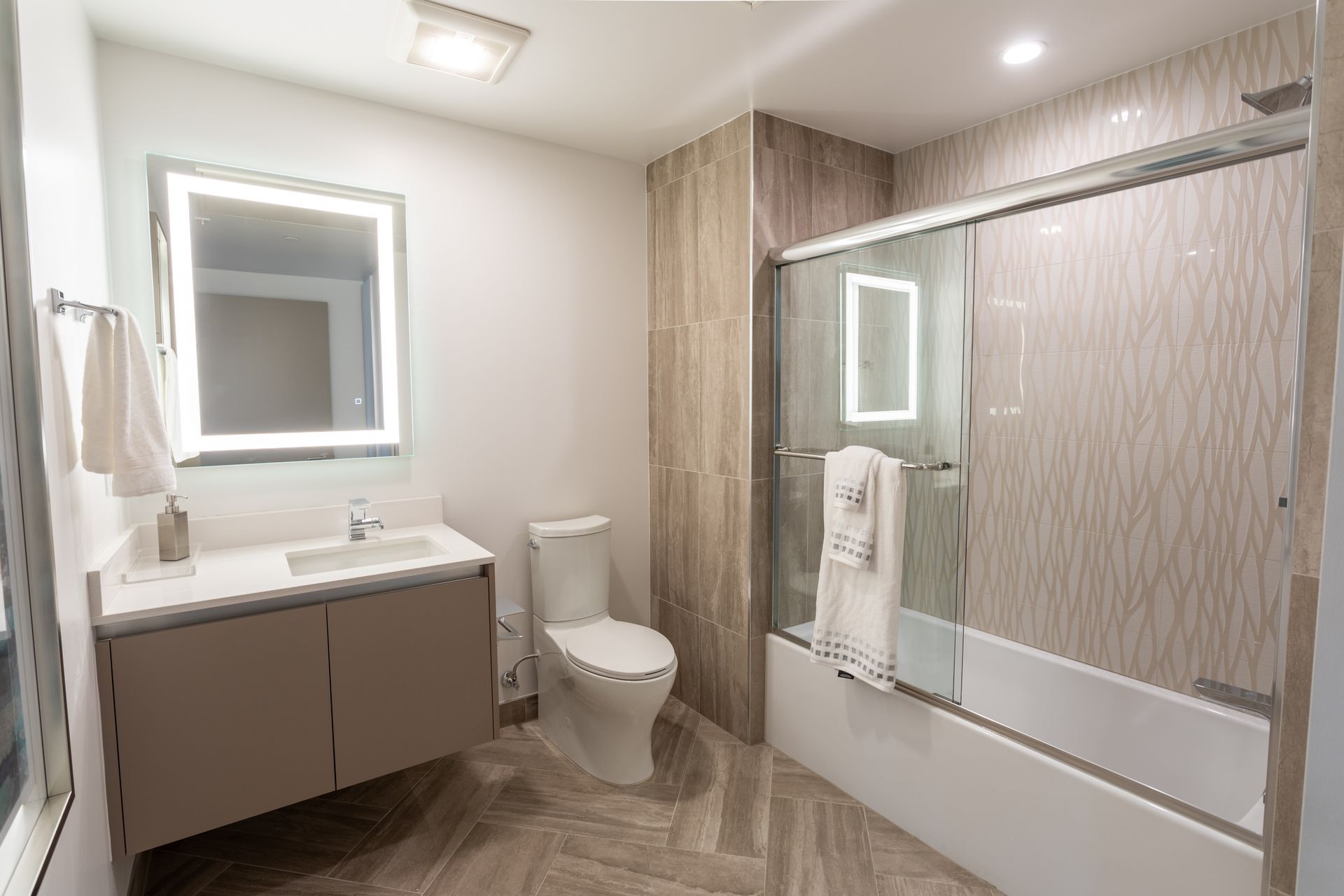 Modern bathroom with a toilet, floating vanity, shower, and a large illuminated mirror.