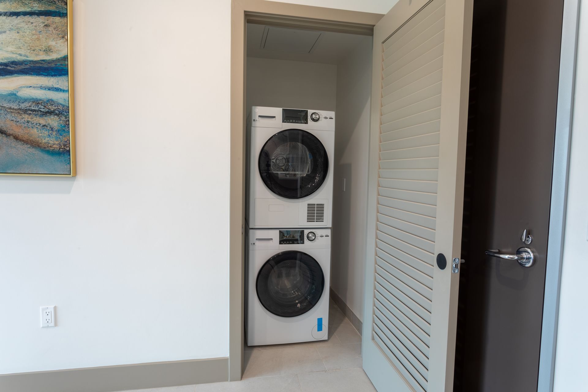 Stackable washer and dryer unit in a closet, next to a partially open, louvered door.