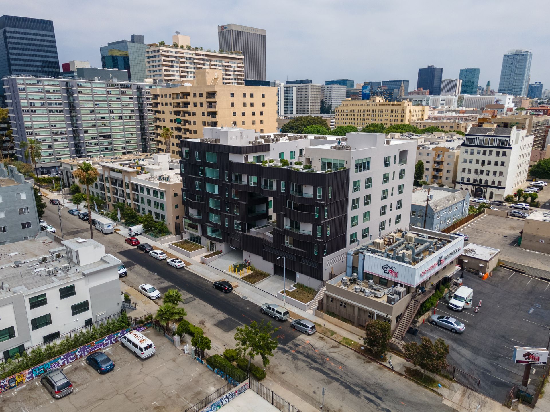 Aerial view of a modern, dark-clad building with a central opening, amidst other buildings and city streets.