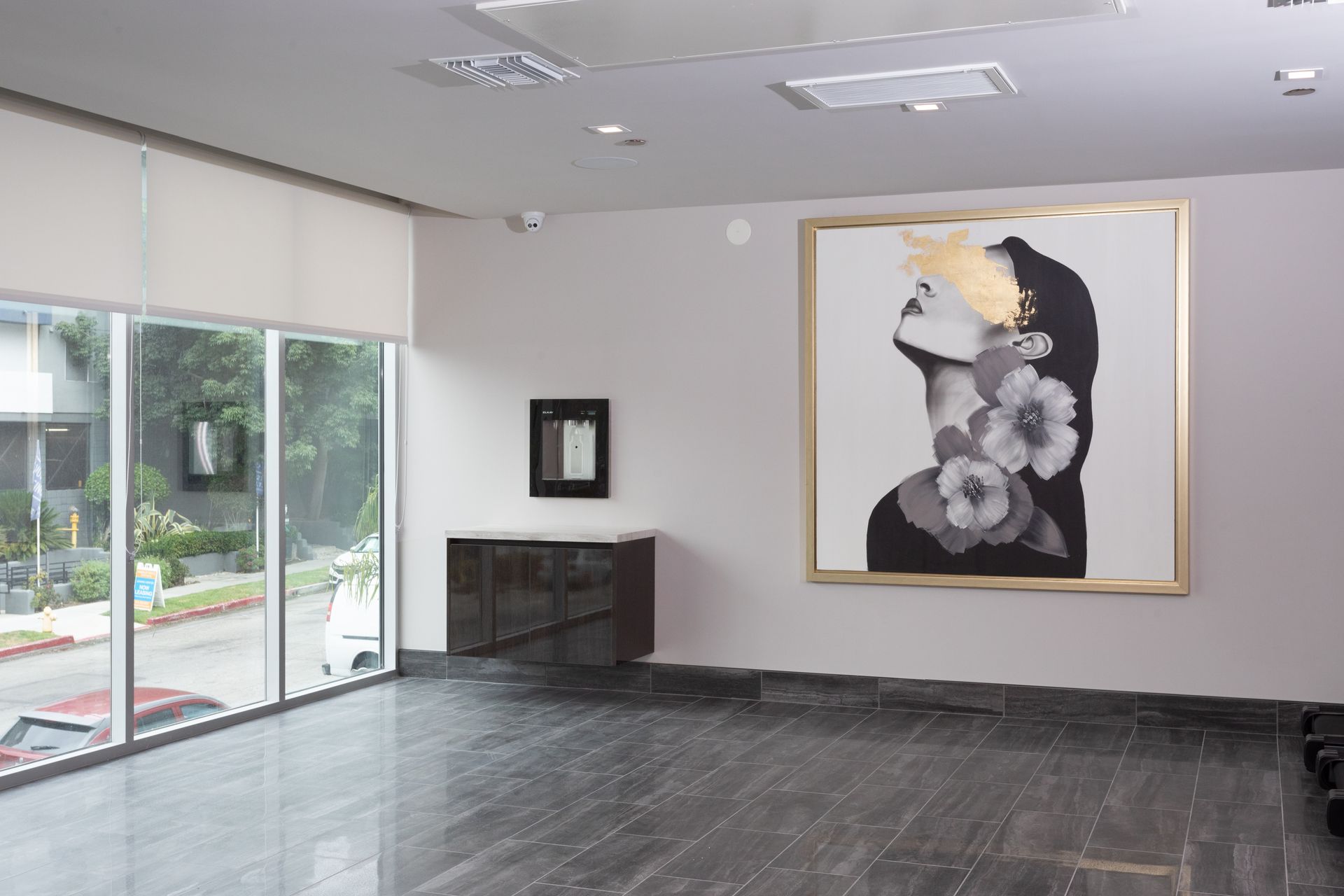Interior art gallery with large portrait, cabinet, windows, and dark flooring.