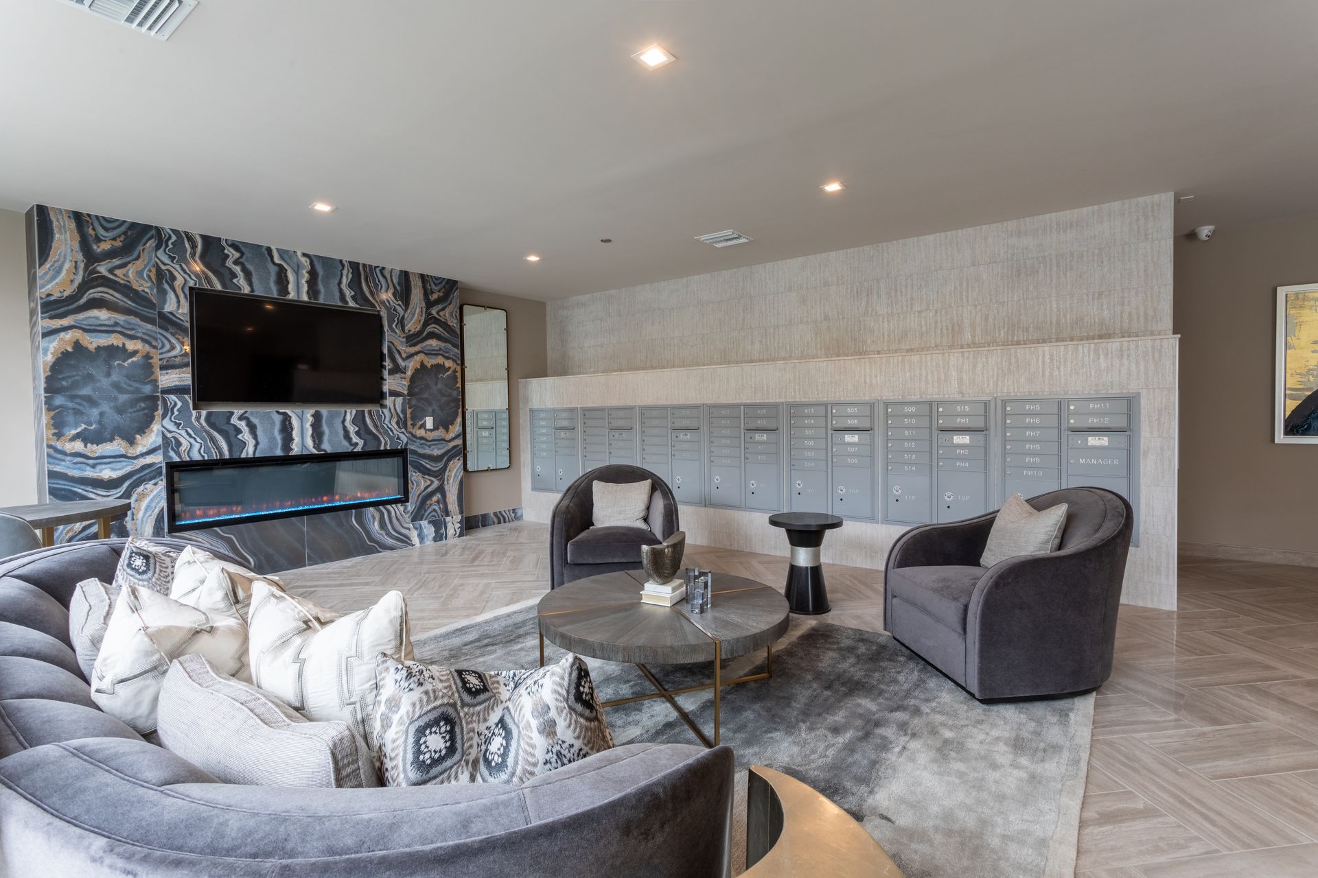 Lounge area with gray sofa, armchairs, fireplace, TV, mailboxes, and coffee table; modern design.