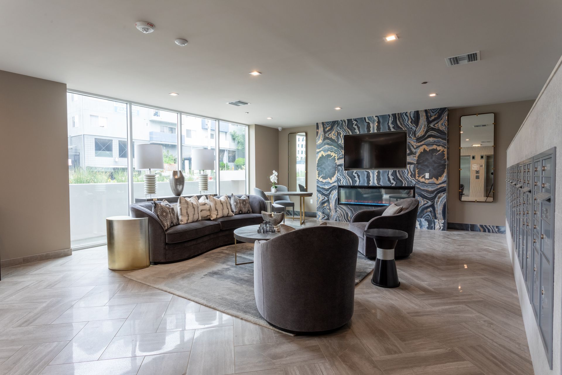 Modern lobby with gray sofa, patterned fireplace, and large windows.