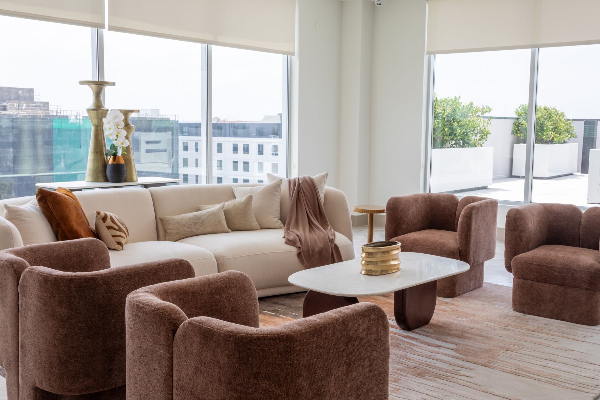 Living room with beige sectional sofa, brown armchairs, and a white coffee table by large windows.