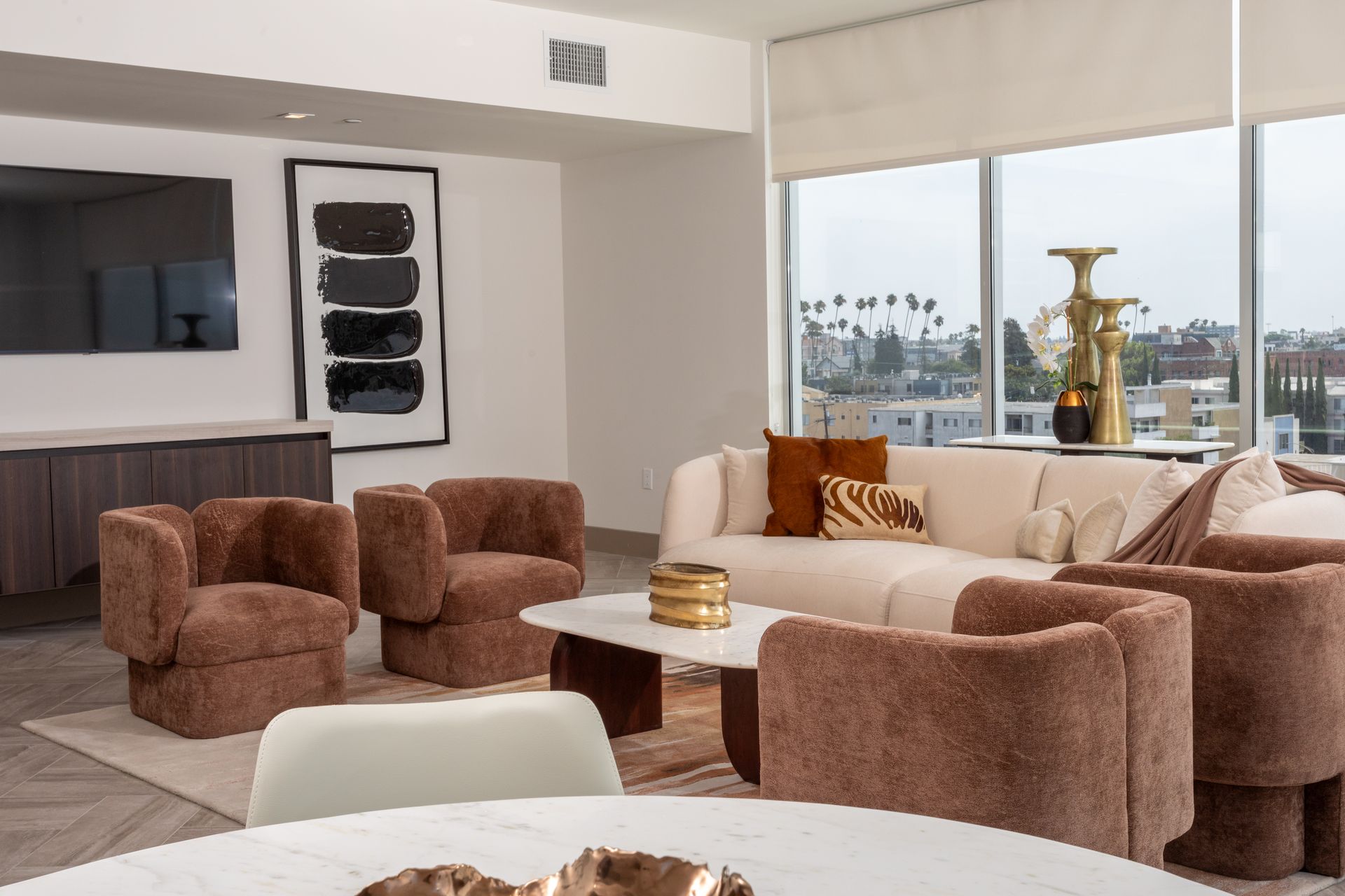 Modern living room with brown and cream furniture, large windows, and artwork.