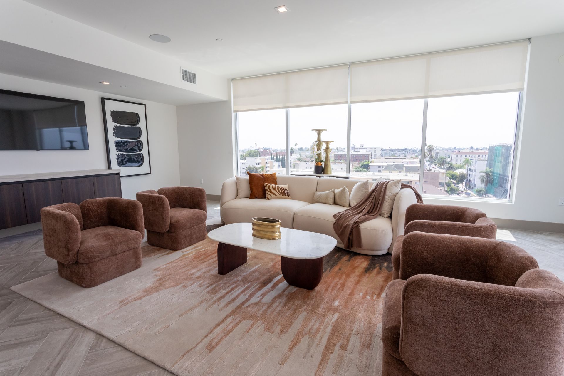 Living room with large windows, cream sofa, brown armchairs, and a marble coffee table.