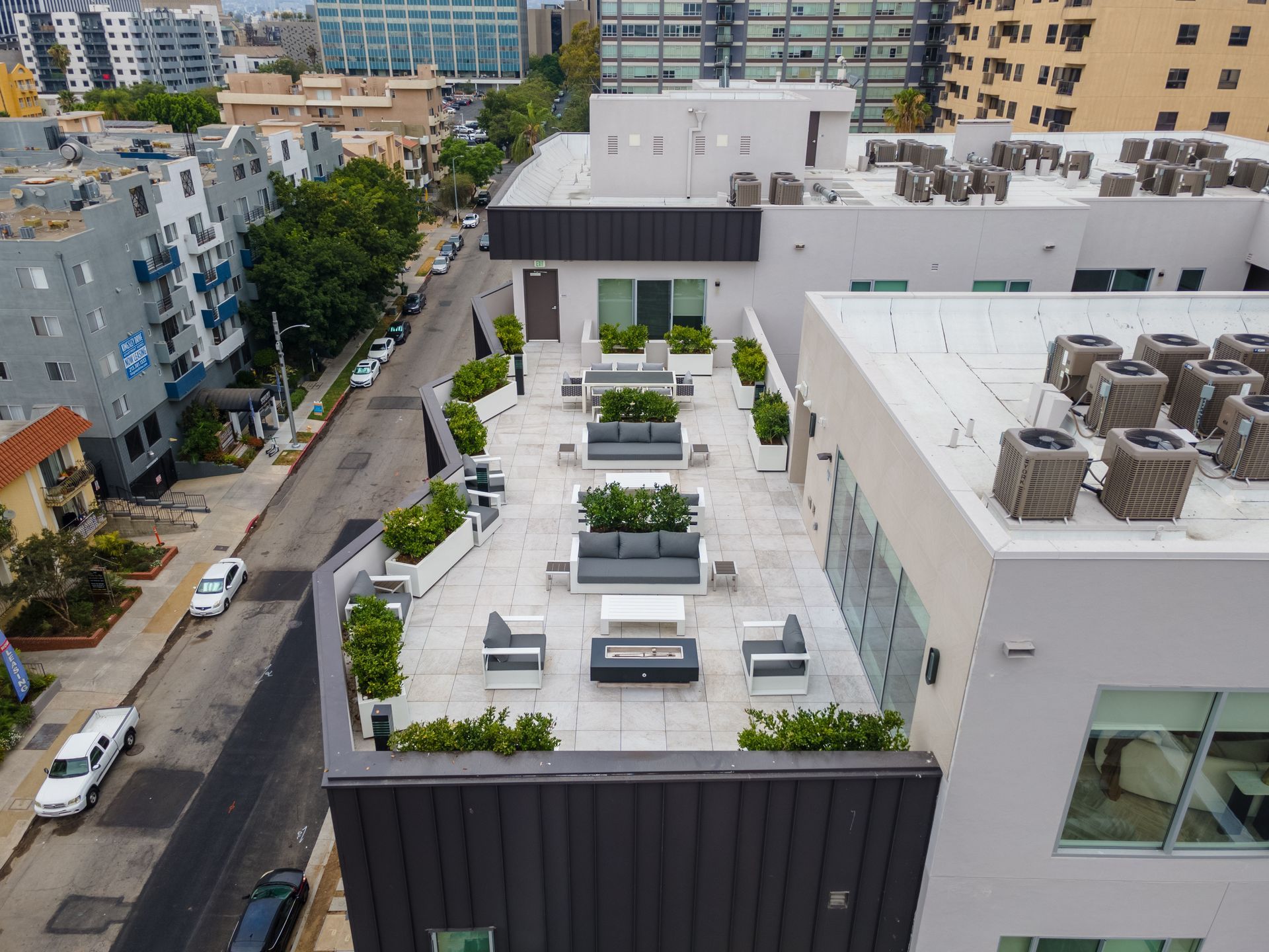 Rooftop patio with seating, plants, and air conditioning units. Street view with cars and buildings.