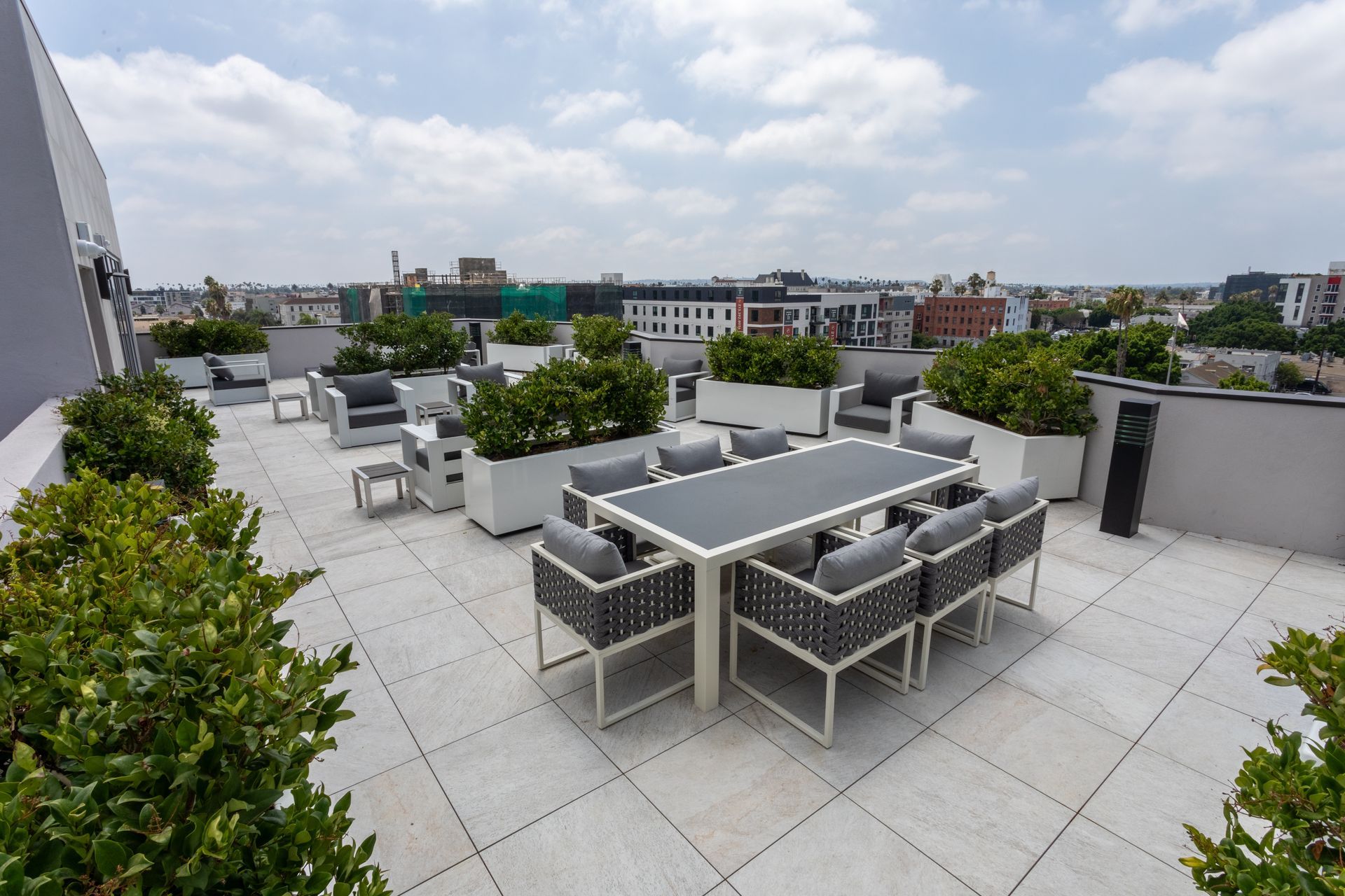 Rooftop patio with modern outdoor furniture, surrounded by greenery and overlooking city buildings.