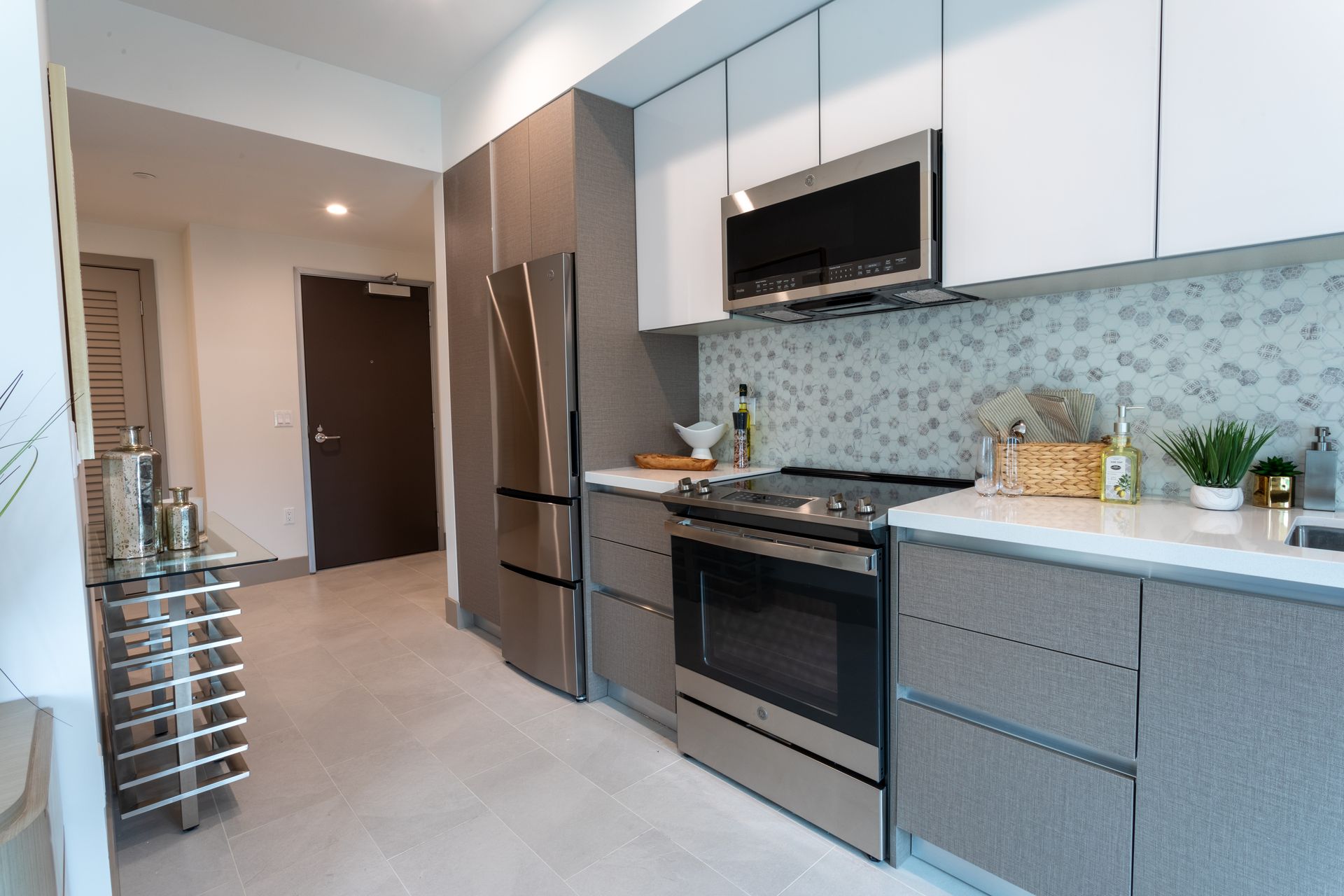 Modern kitchen with stainless steel appliances, grey cabinets, white countertops, and decorative backsplash.