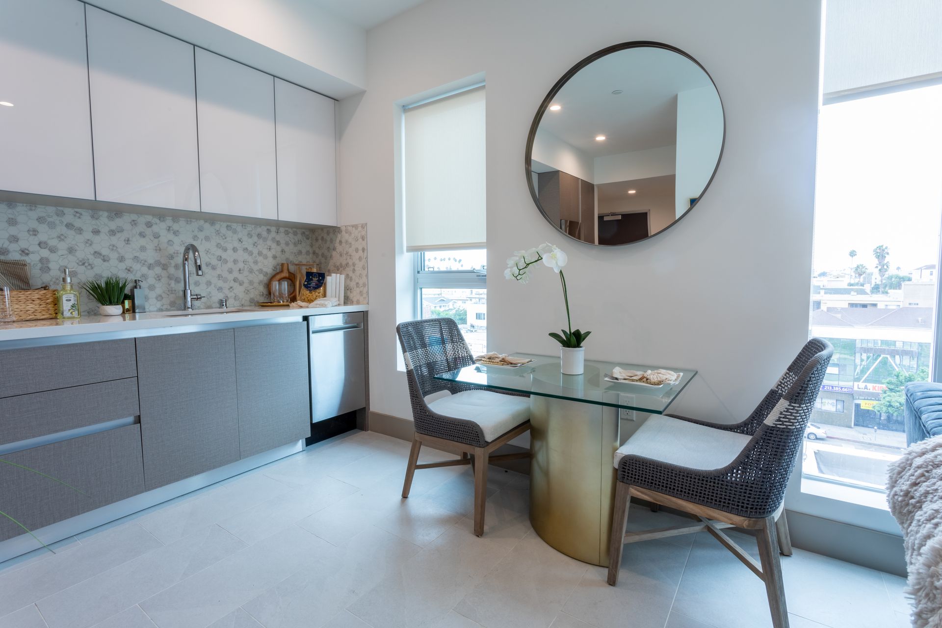 Modern kitchen with light gray cabinetry, stainless steel appliances, and a small dining table with two chairs.